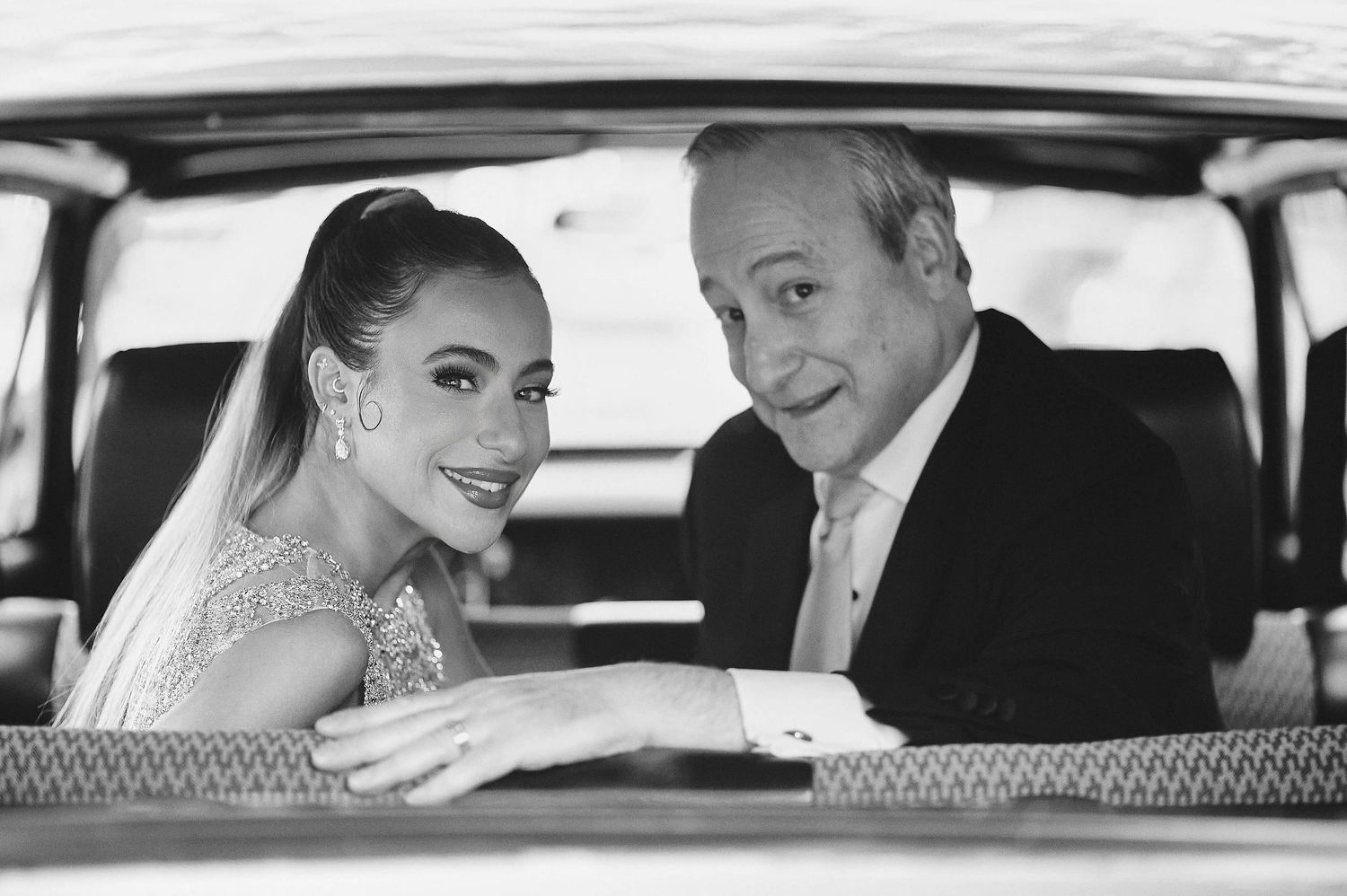 A black and white wedding photo shows a couple smiling together in a classic car.