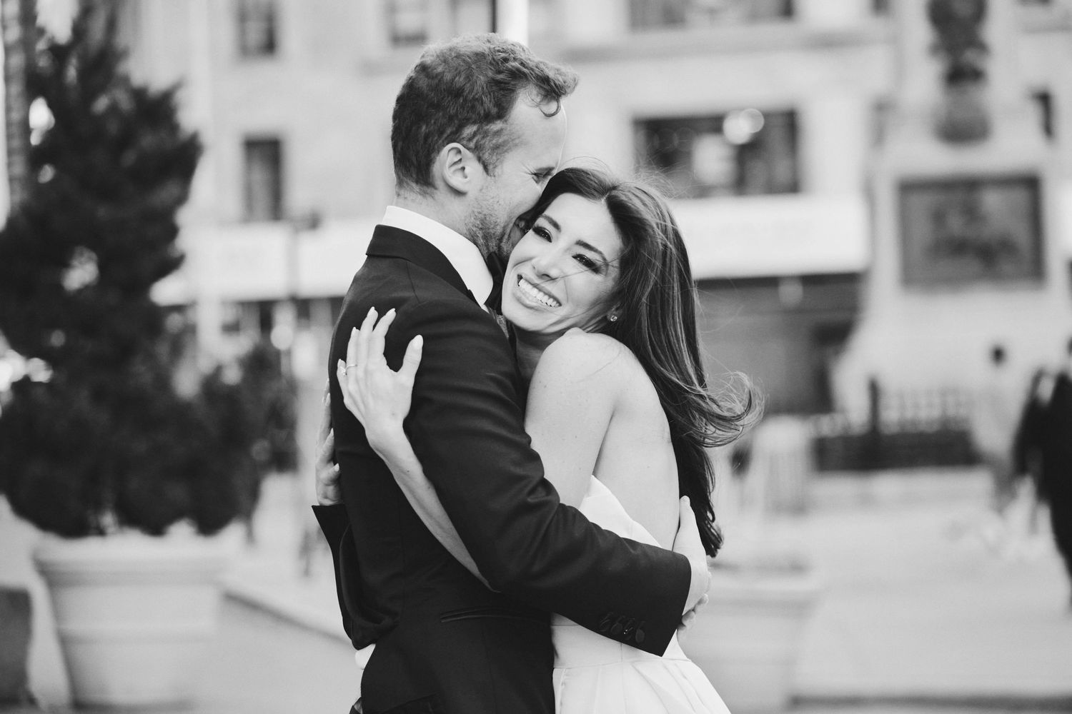 A joyful couple embraces and laughs together on a city street in black and white photography.