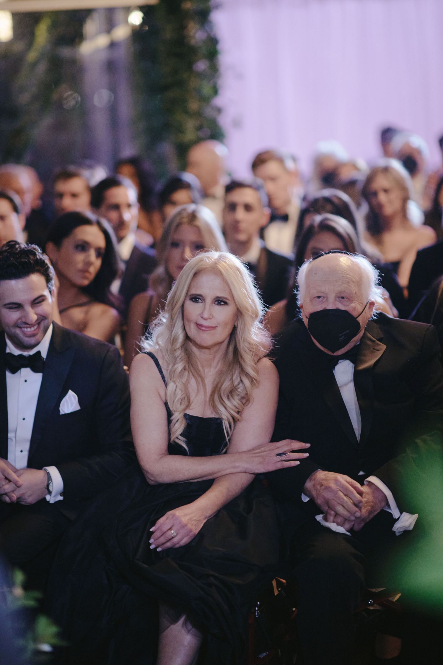 Formal event attendees in black tie attire sit together in an audience during an elegant evening gathering.