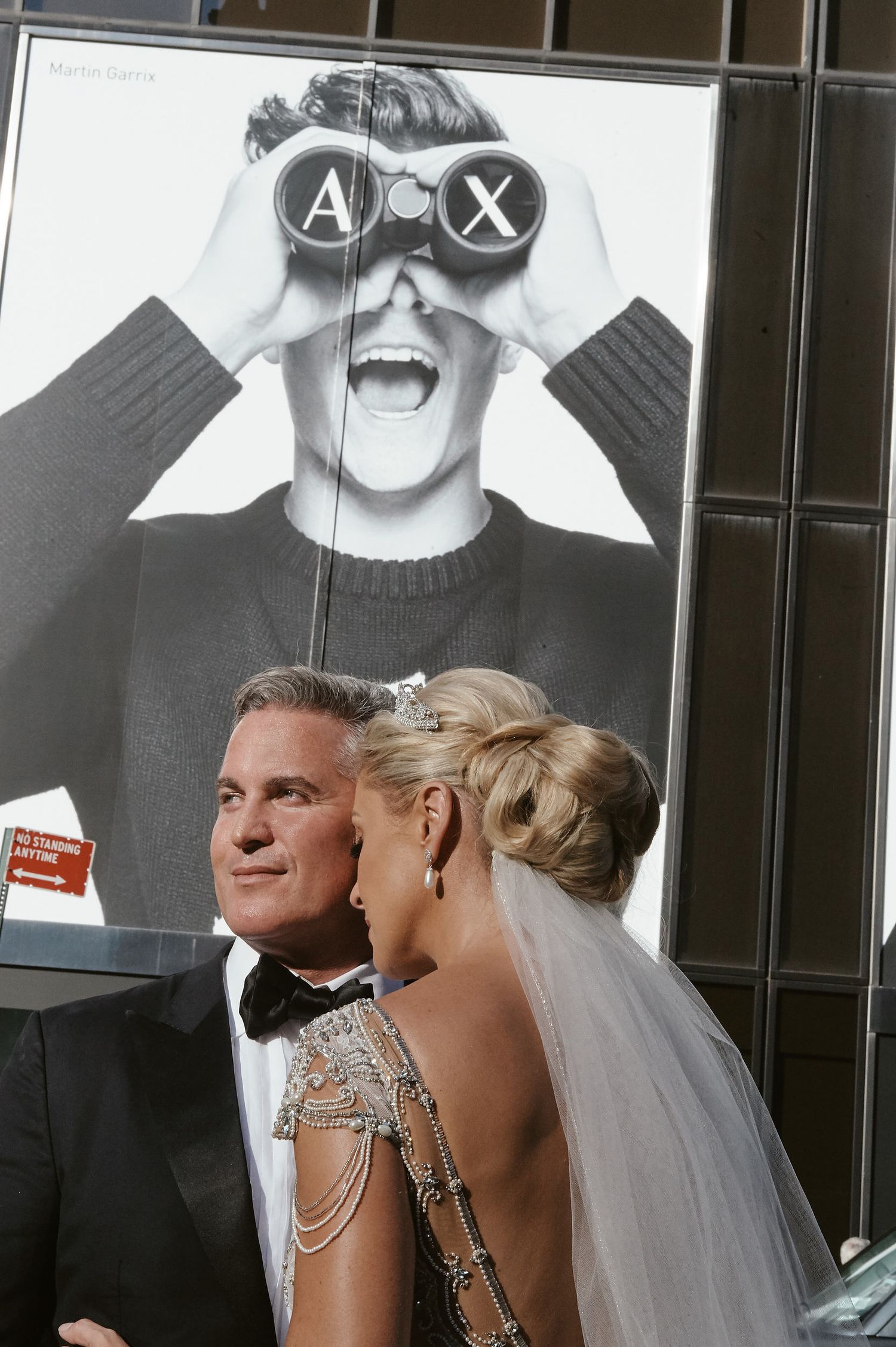 A wedding couple stands in front of a large black and white fashion advertisement on a building exterior.