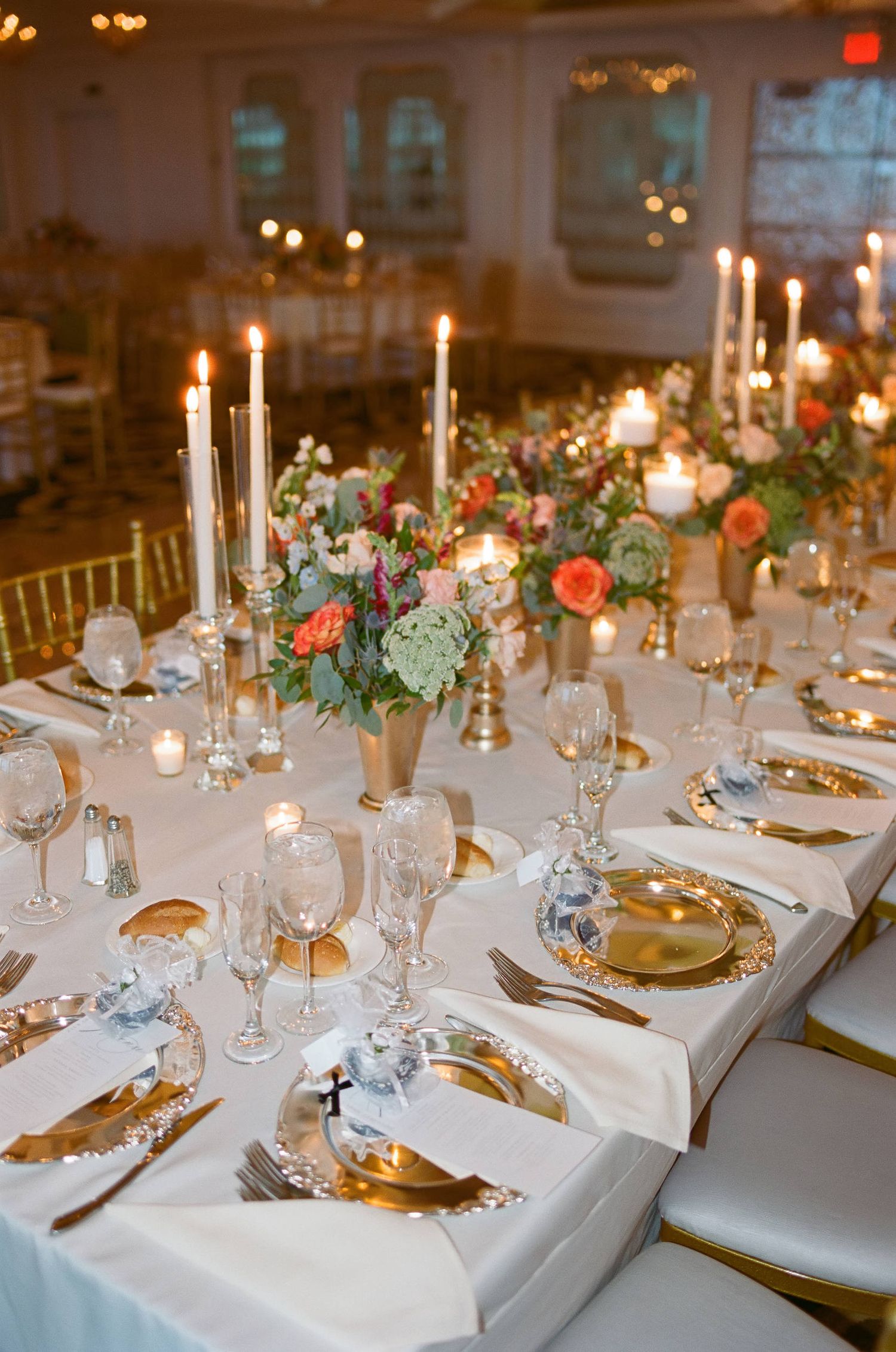 Romantic wedding reception table with candlelight, floral centerpieces, and gold accented place settings.