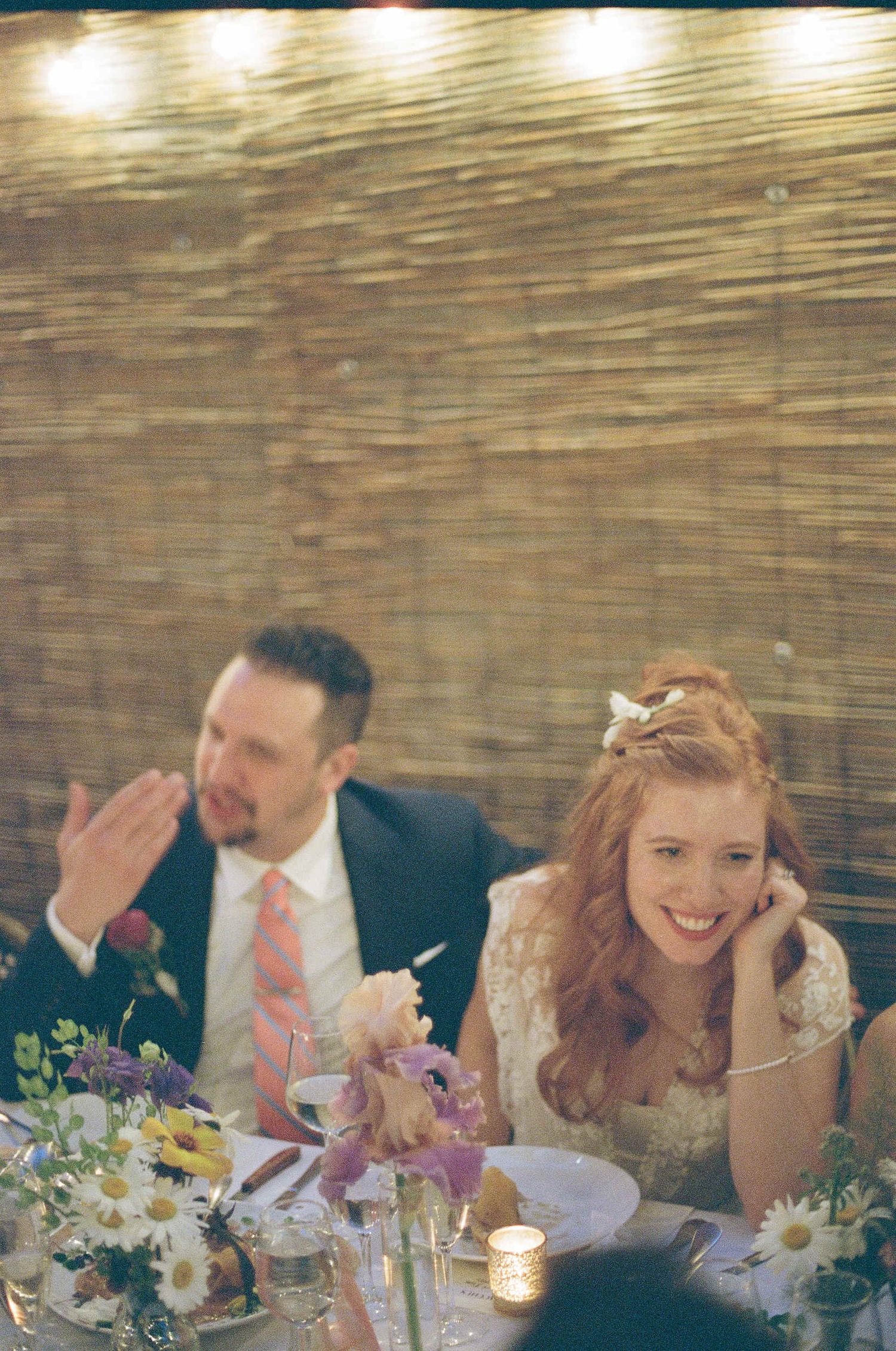 Wedding couple shares a candid moment at their reception table decorated with daisies and candlelight.