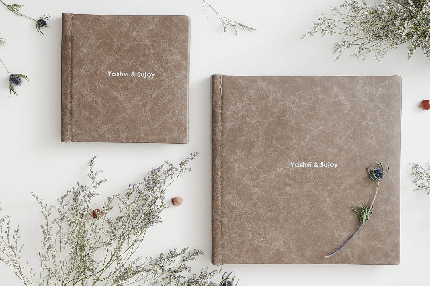 Two brown leather wedding photo albums with delicate dried flowers laid on white background.