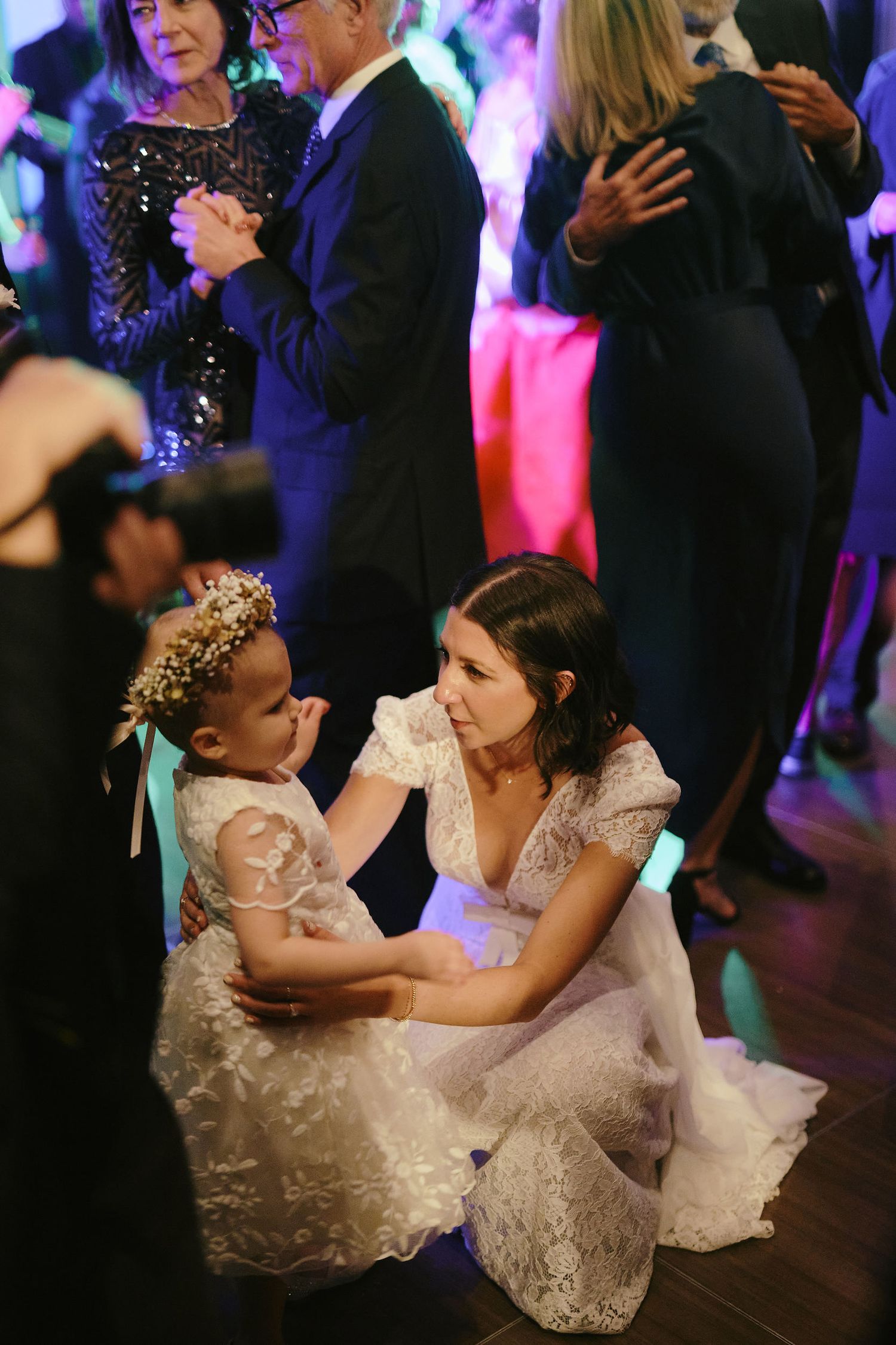 A sweet moment between a flower girl in a sparkly dress and tiara dancing with a woman in lace at a wedding reception.