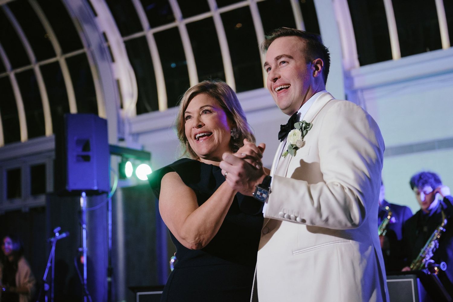 Two people share a joyful dance moment at an elegant indoor reception with a band performing in the background.