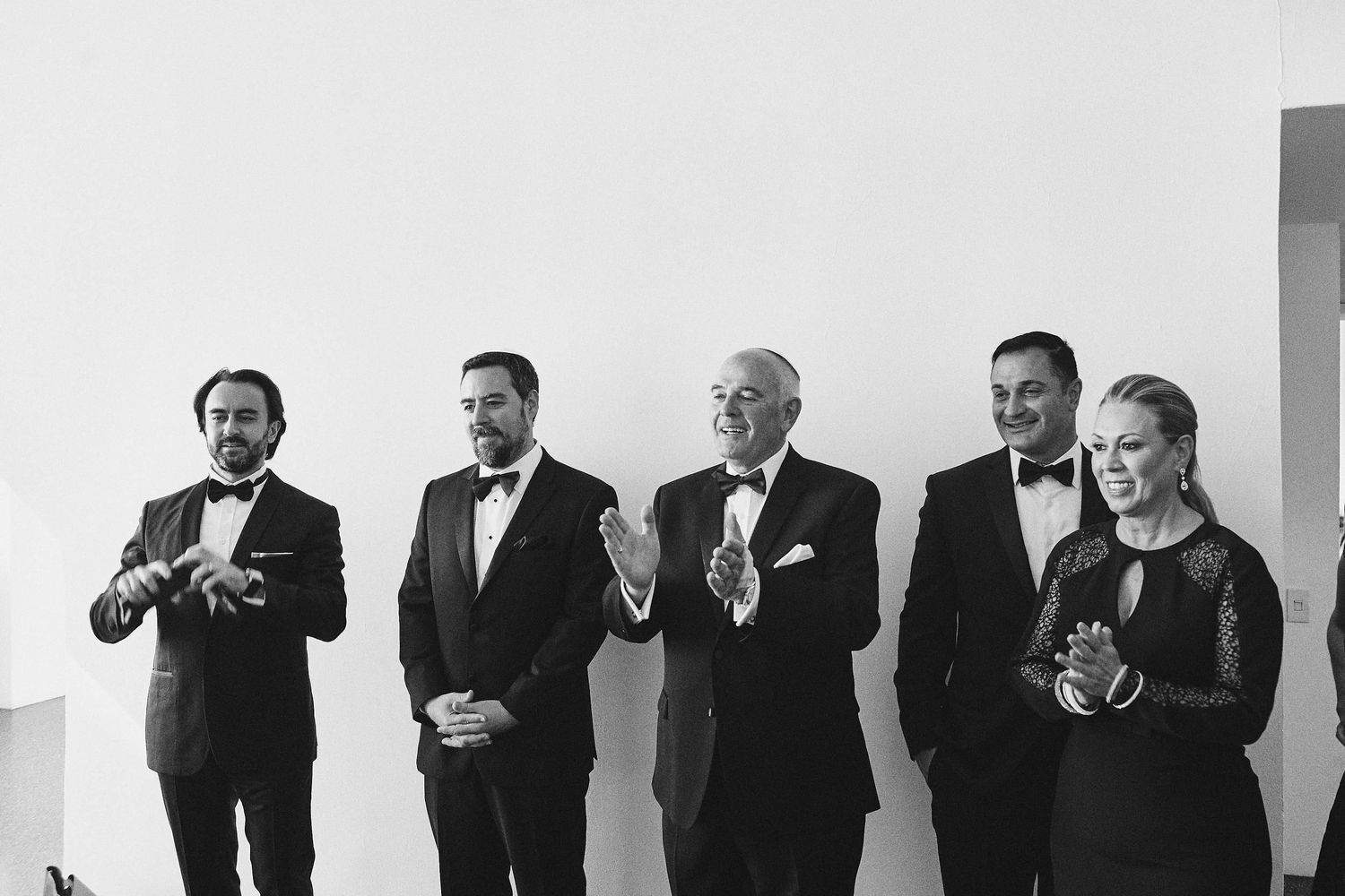 A black and white photo of five men in formal attire toasting with drinks at an elegant gathering.