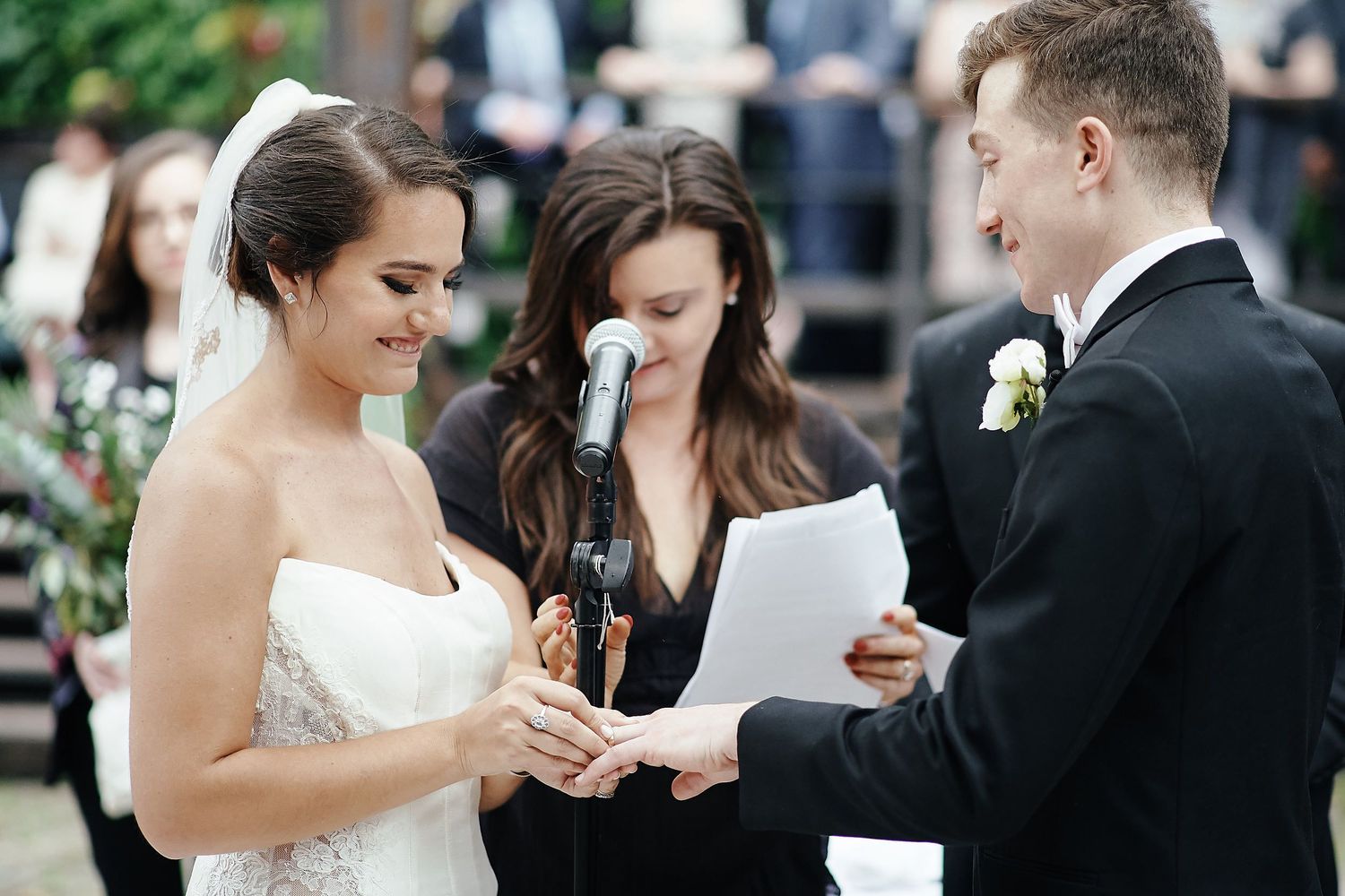 A couple exchanges vows during an outdoor wedding ceremony as an officiant reads from a document.