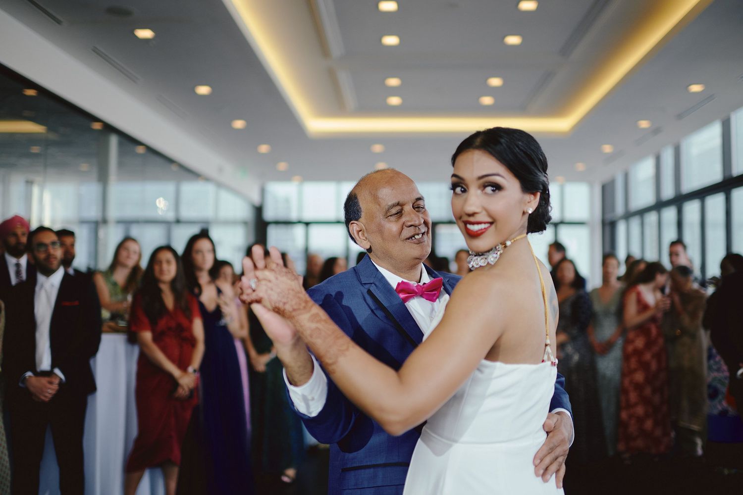 Two people sharing a joyful dance moment at a formal event with guests watching in a bright indoor venue.