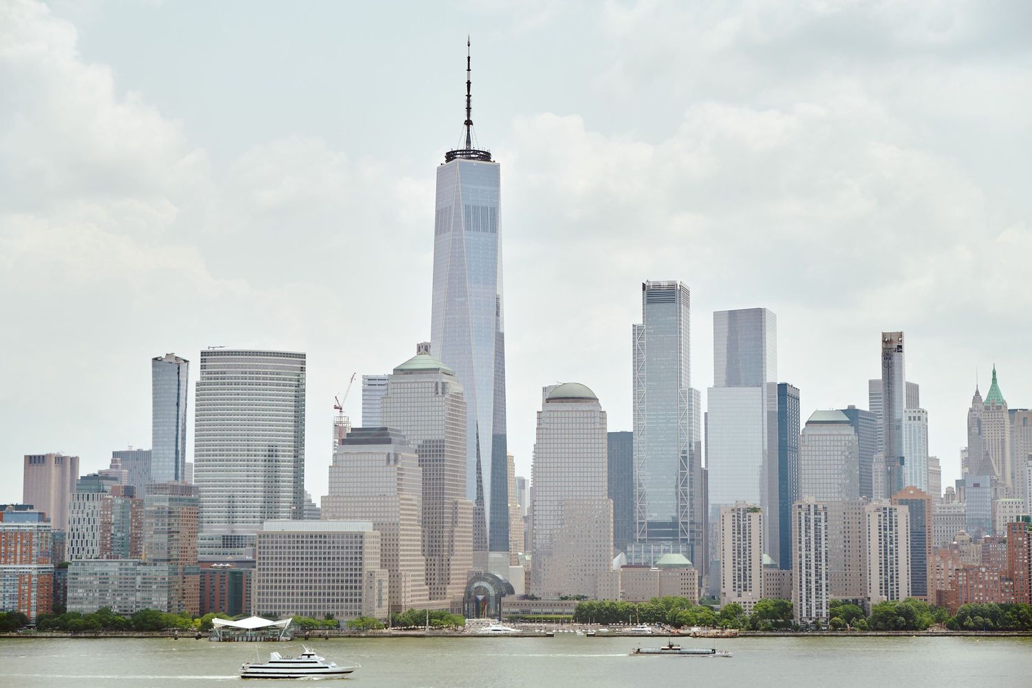 Manhattan skyline featuring One World Trade Center and modern skyscrapers viewed across the Hudson River on a cloudy day.