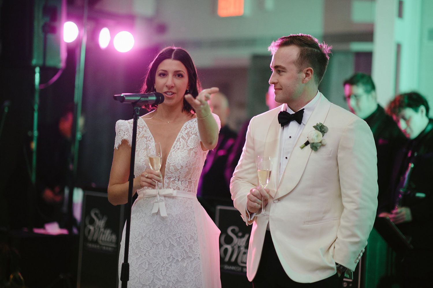 Performers sing during wedding entertainment at venue with pink and purple mood lighting.