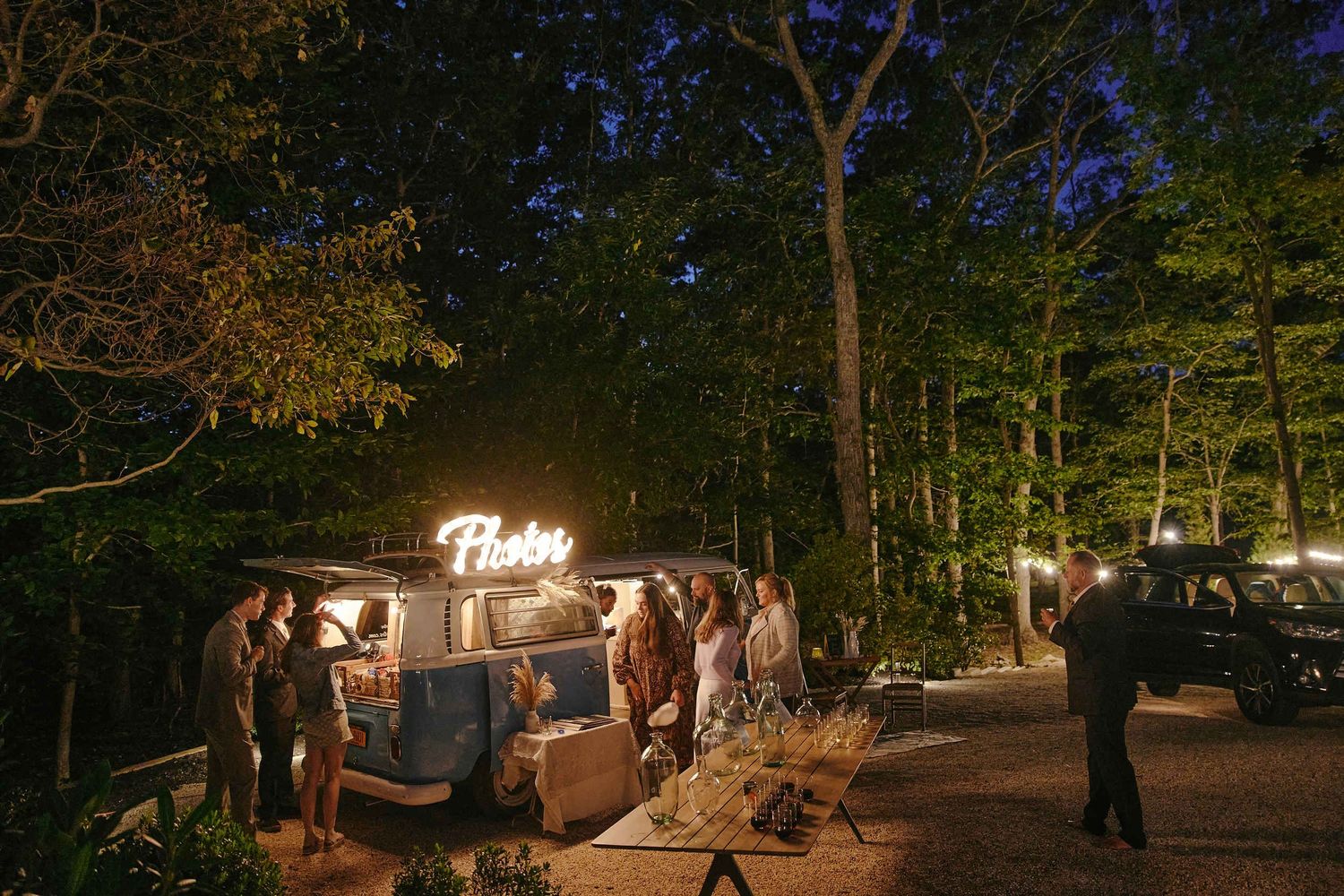 Food truck at a nighttime outdoor wedding reception with guests gathered under string lights in a wooded setting.