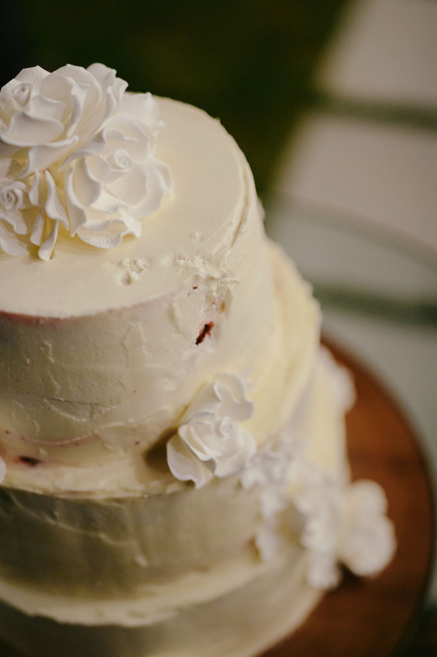 Elegant white wedding cake with delicate sugar roses and smooth buttercream frosting photographed in soft focus.