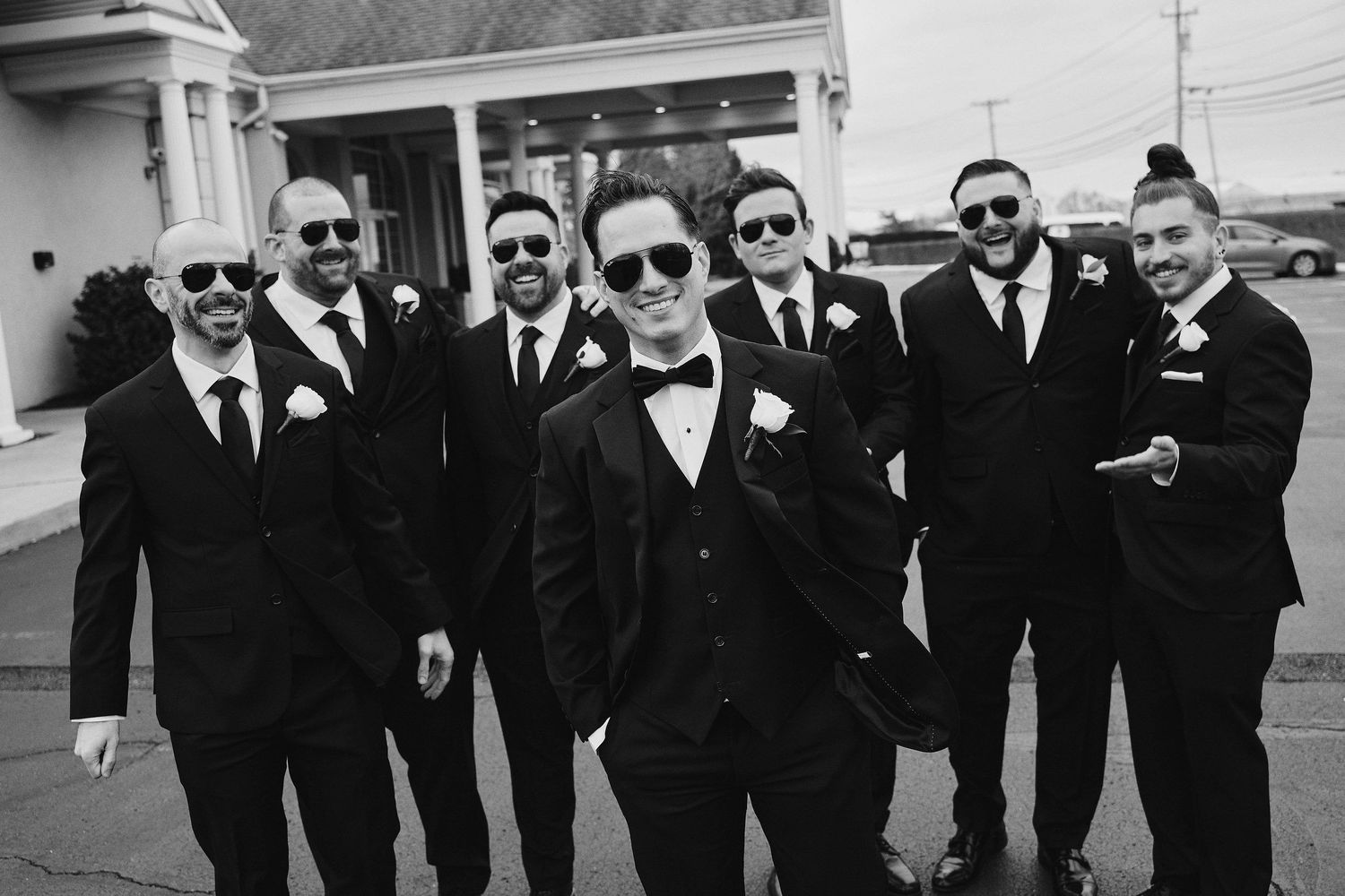Black and white photo of groomsmen in matching black suits and sunglasses posing together outdoors on wedding day.
