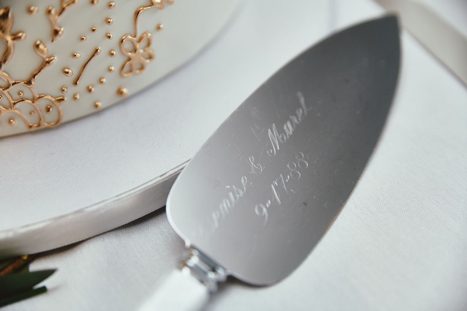 Silver cake server with engraved calligraphy text displayed on white surface next to floral decor.