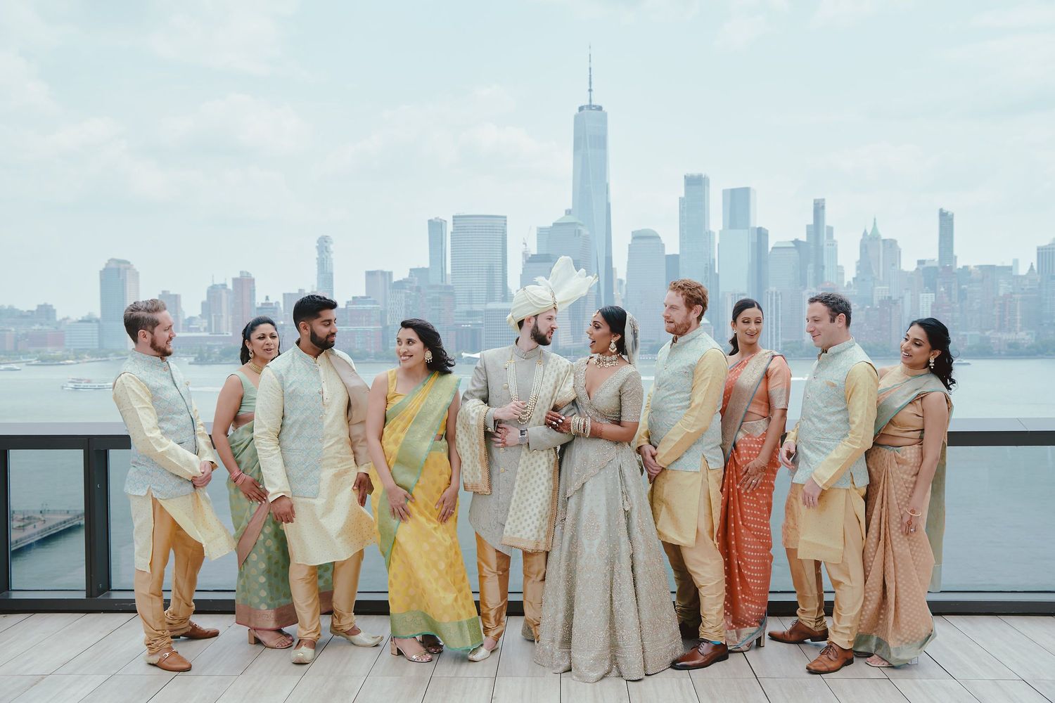 Wedding party in pastel Indian attire posed together with Manhattan skyline view.