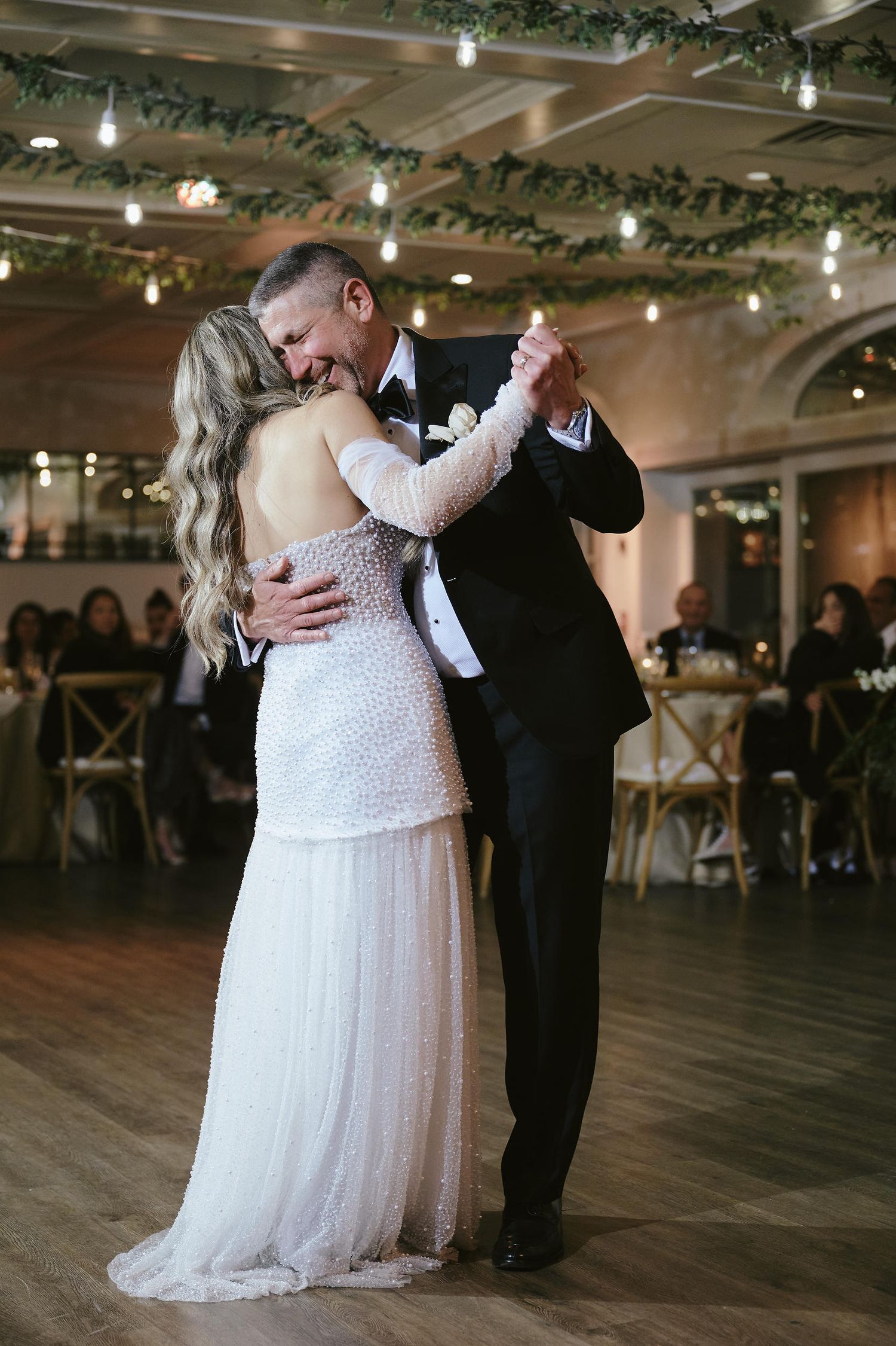 A couple shares an intimate first dance at their wedding reception under romantic lighting and greenery decorations.
