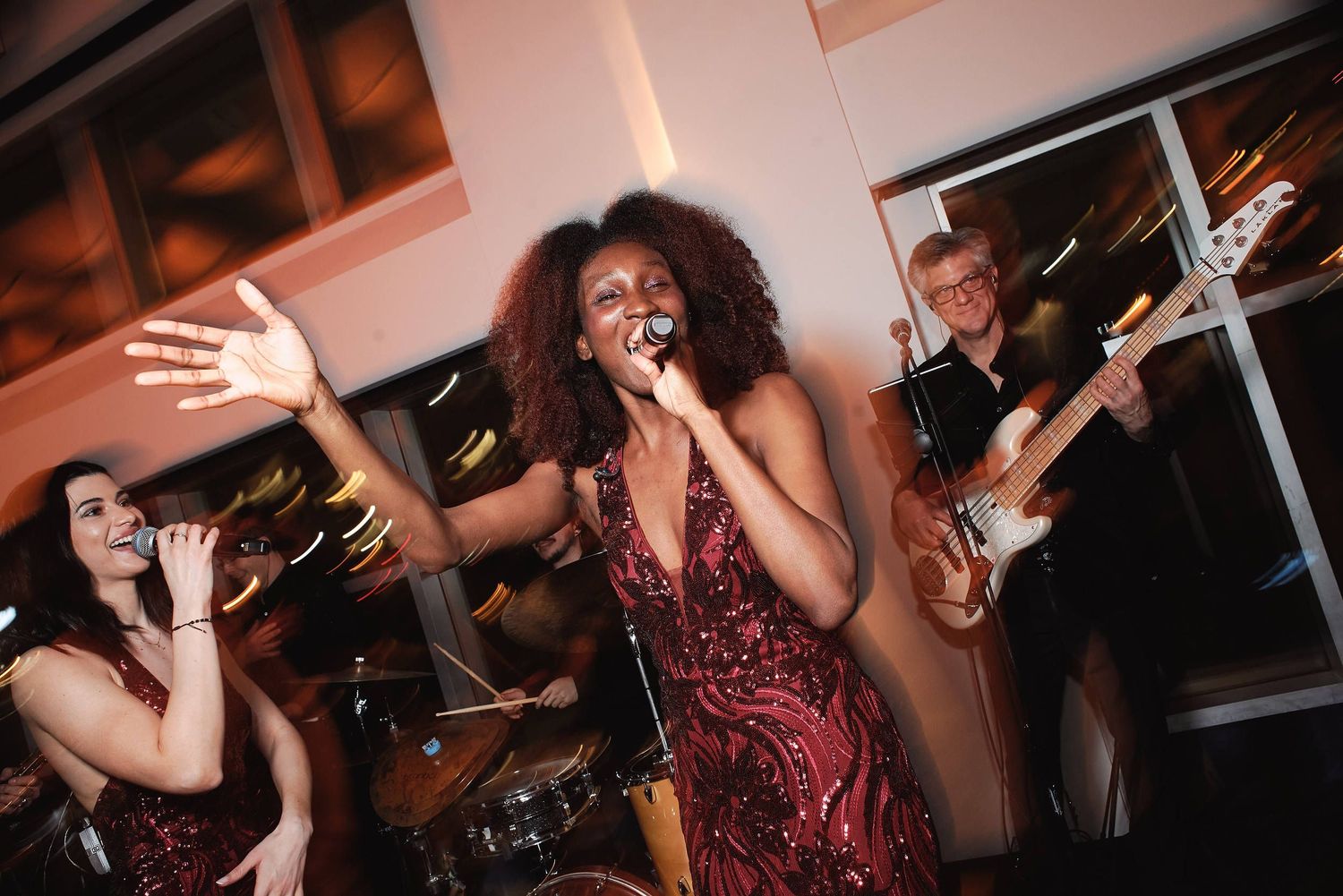 Energetic live band performance with lead singer in red sequin dress singing passionately while musicians play in background.