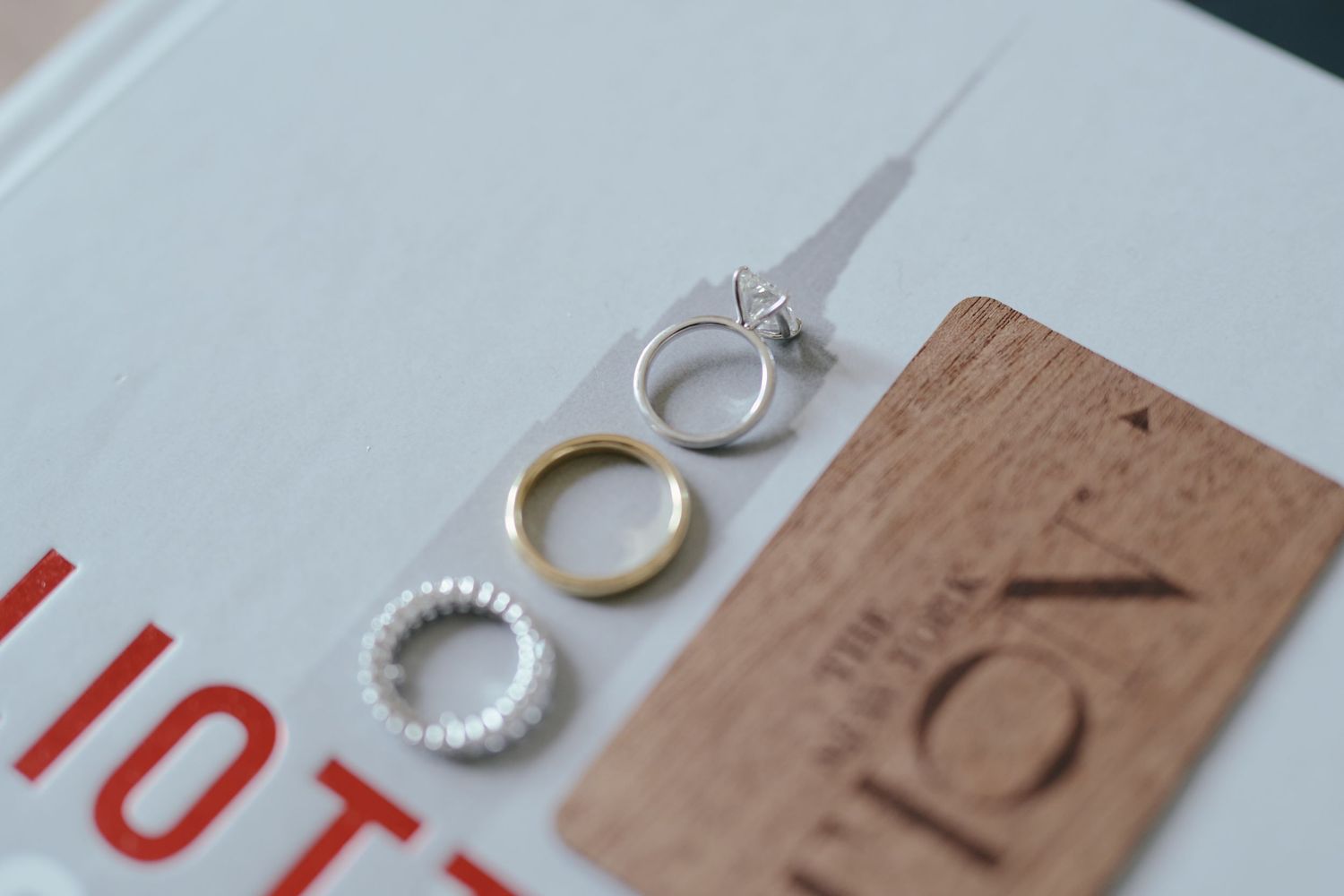 Three different wedding rings including silver, gold and pearl bands displayed next to a wooden card on white surface.