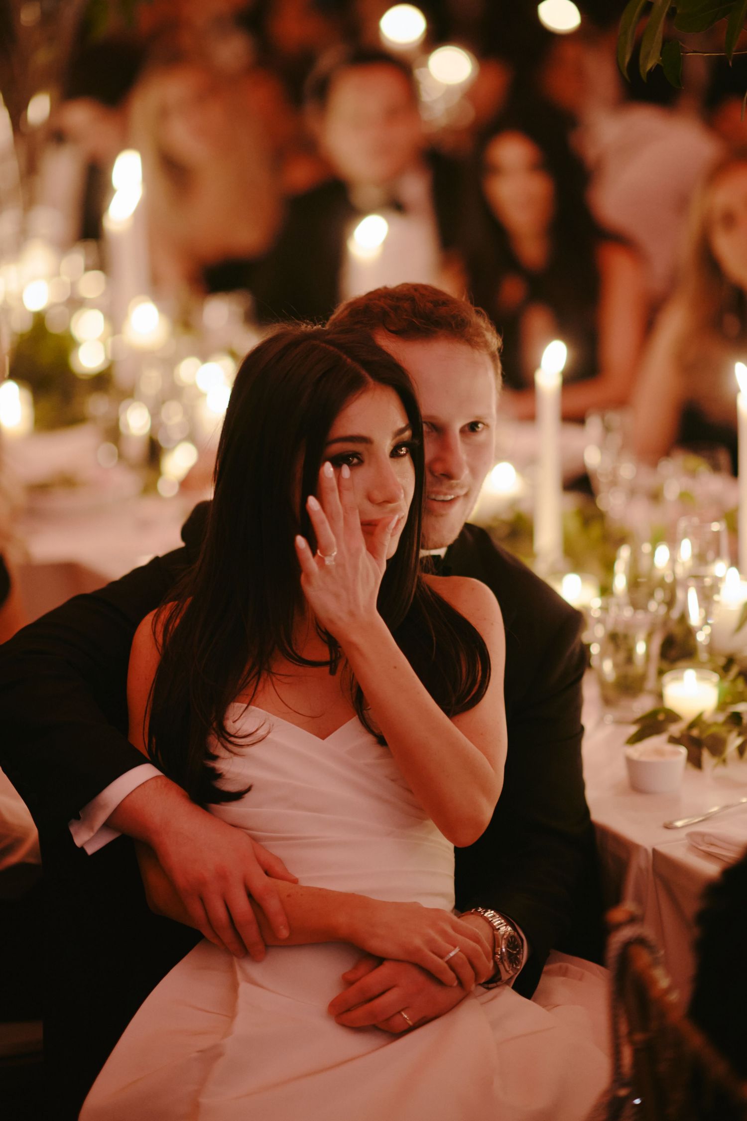 A couple shares an intimate moment at an elegant candlelit wedding reception with romantic ambient lighting.