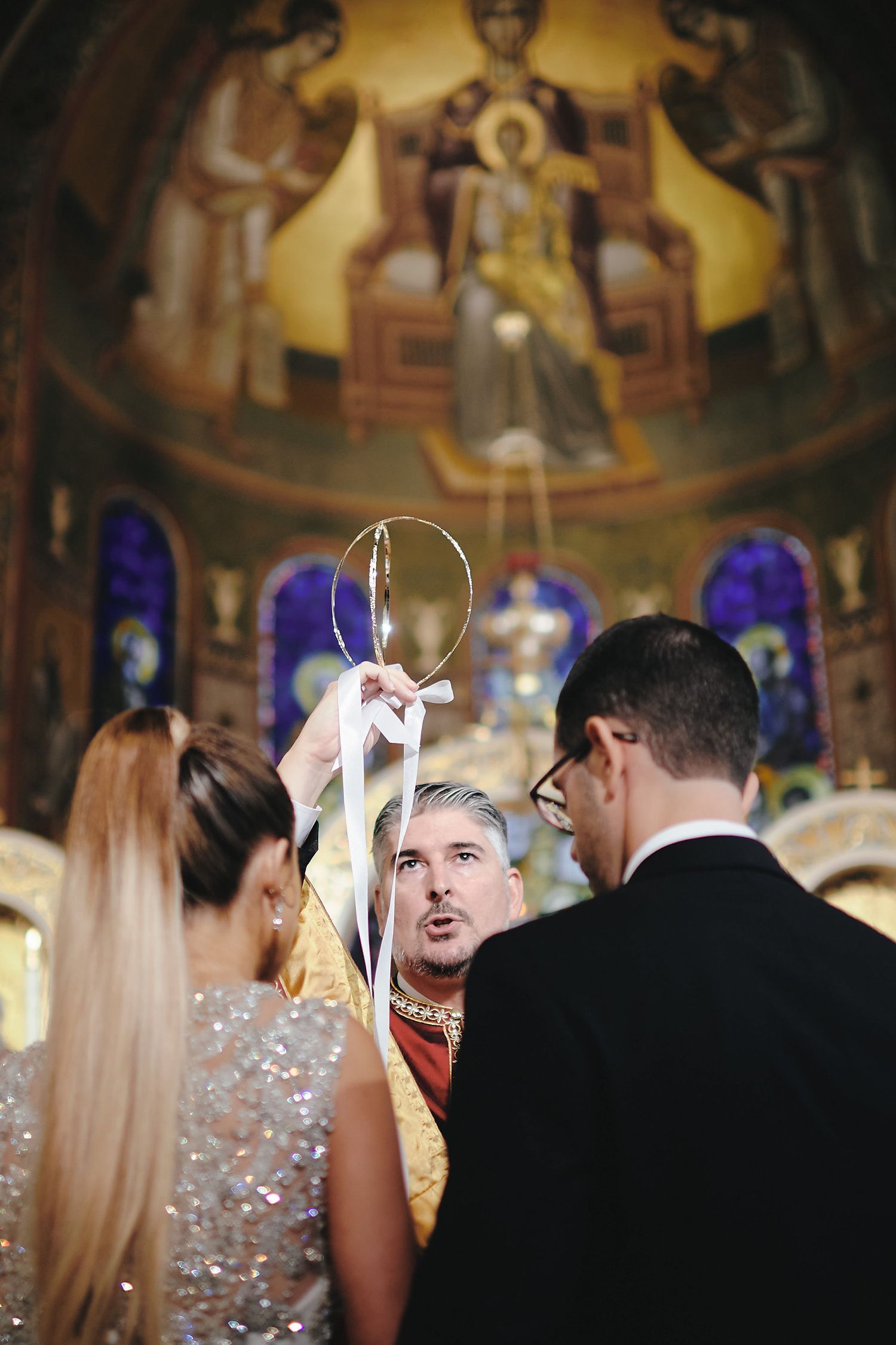 Orthodox wedding ceremony takes place in ornate church with stained glass windows and religious iconography in background.