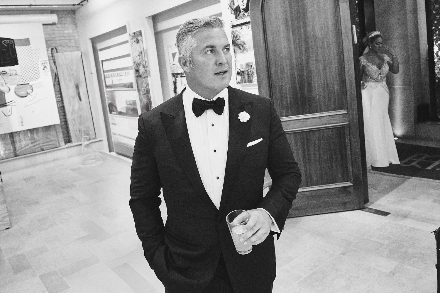 Person in a classic black tuxedo with bow tie standing in an elegant interior hallway.
