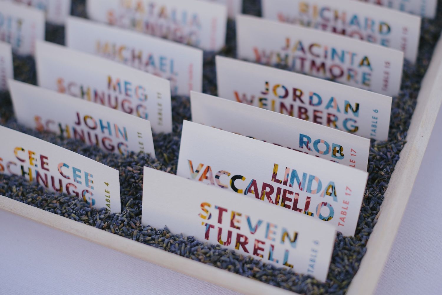 White name place cards with gold foil lettering arranged in neat rows on dark textured surface.