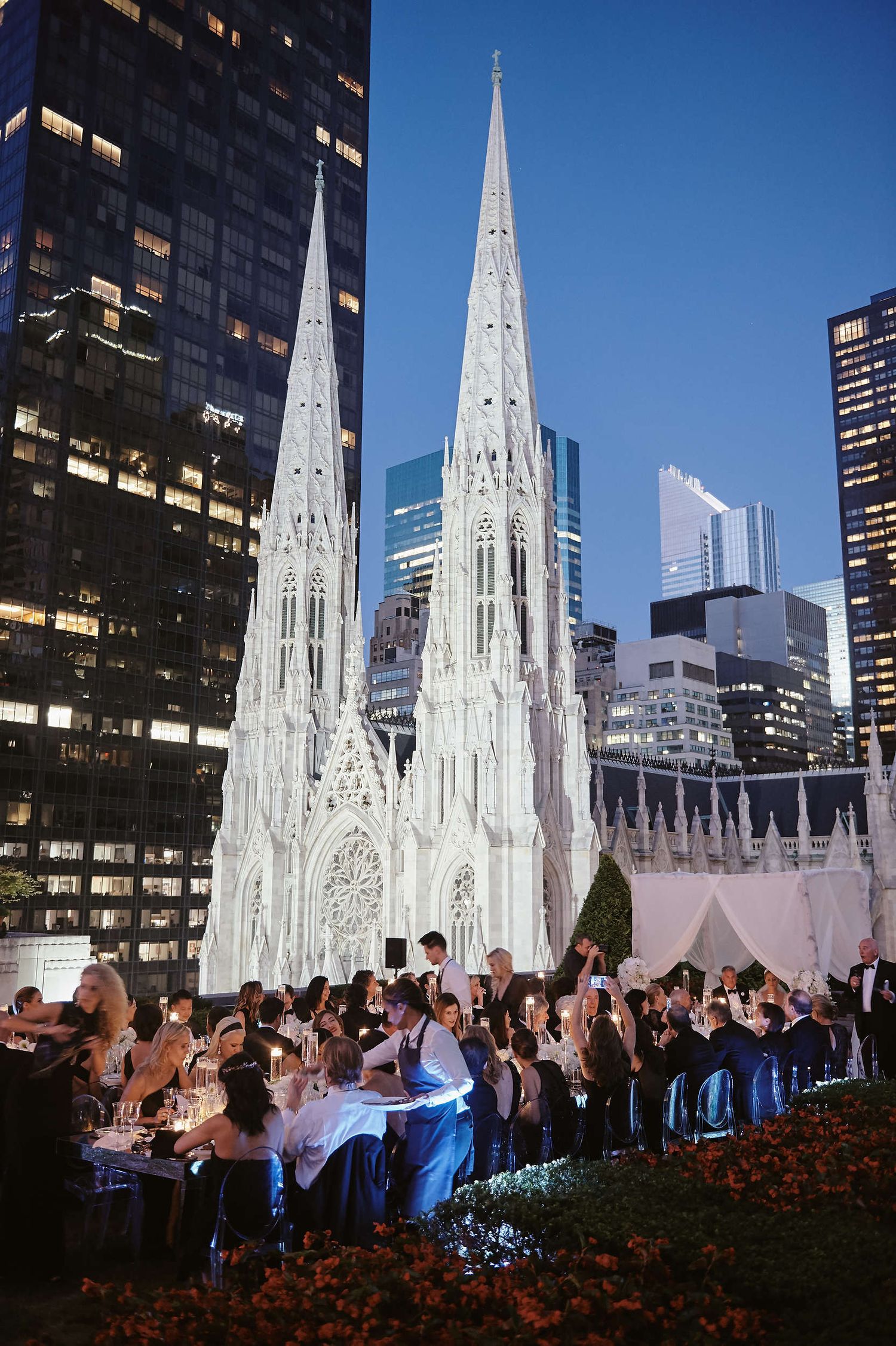 A Wedding reception setup in front of Saint Patrick's Cathedral in New York City at dusk with illuminated spires.