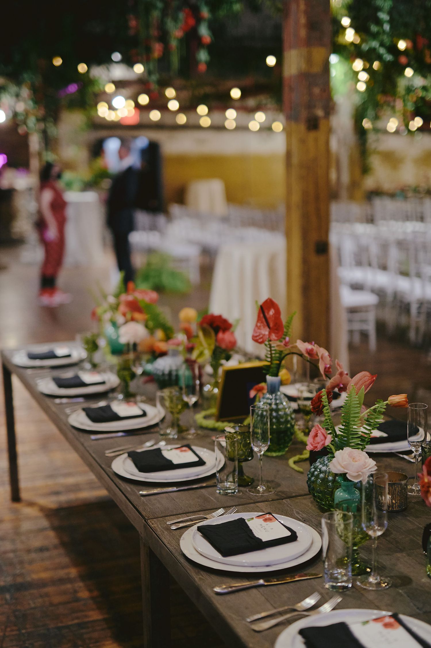 Rustic wooden table set for wedding dinner with elegant place settings and blue mason jar centerpieces with flowers.