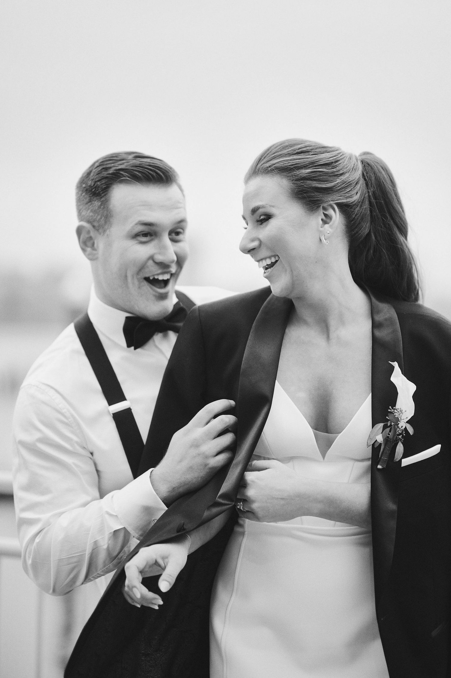 Black and white photo of a joyful couple laughing together on their wedding day, dressed in formal attire.