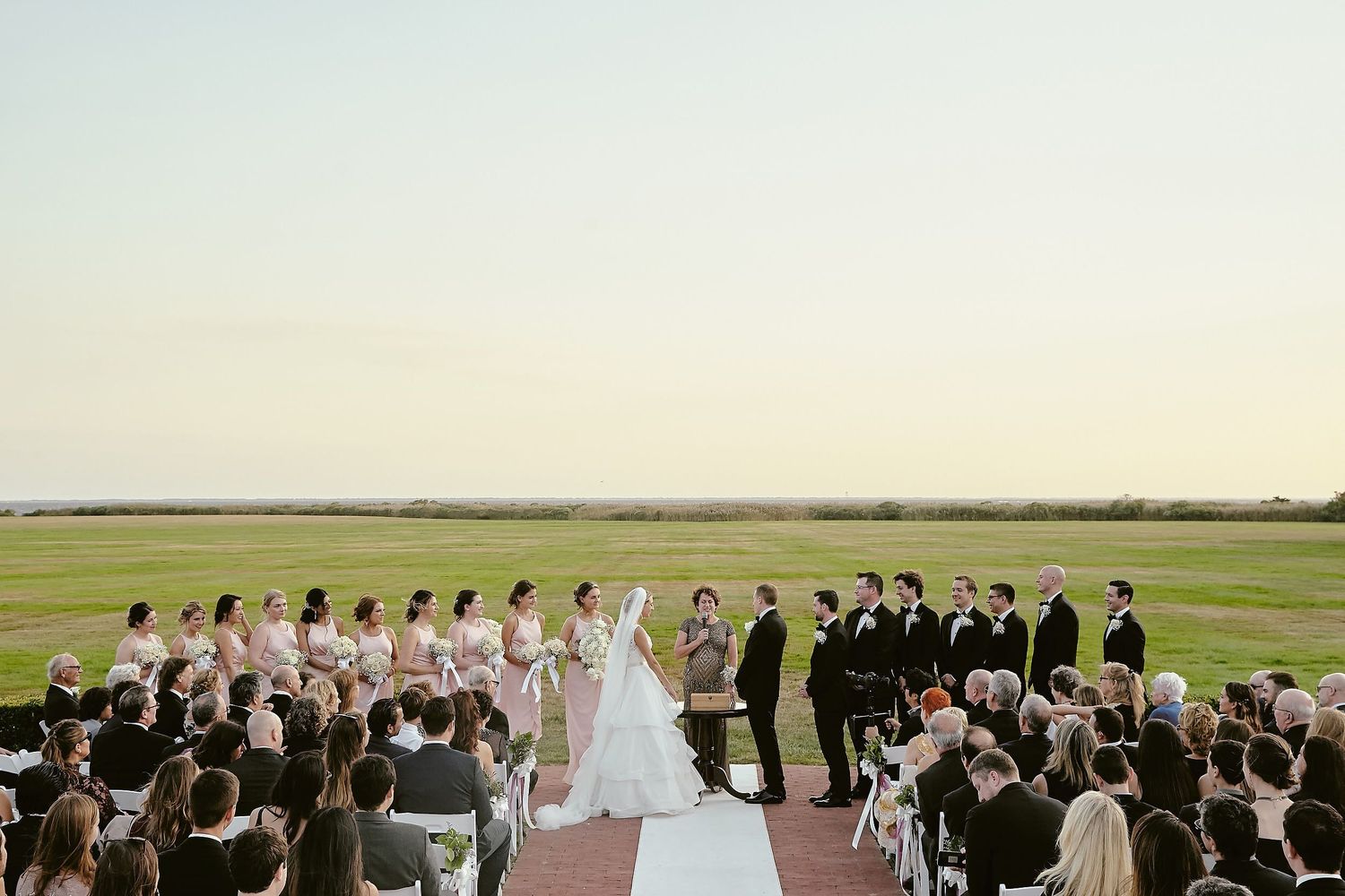 An outdoor wedding ceremony overlooking expansive coastal views with guests seated on either side of the aisle.