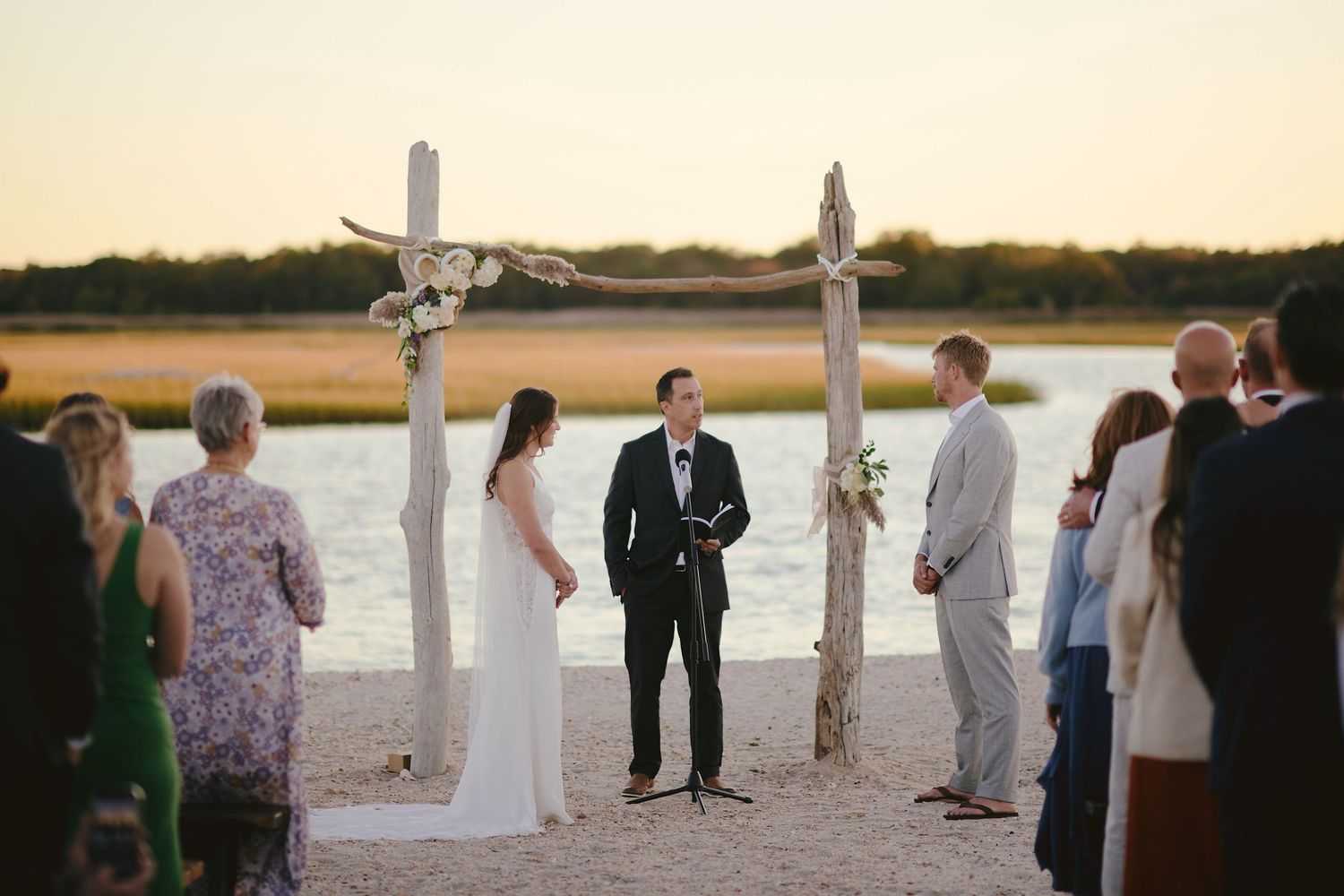 A seaside wedding ceremony at sunset with wooden cross arbors and guests gathered on the beach.