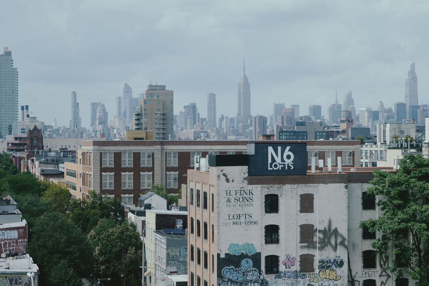 Urban cityscape of New York City skyline with old brick buildings in foreground and modern skyscrapers in background.