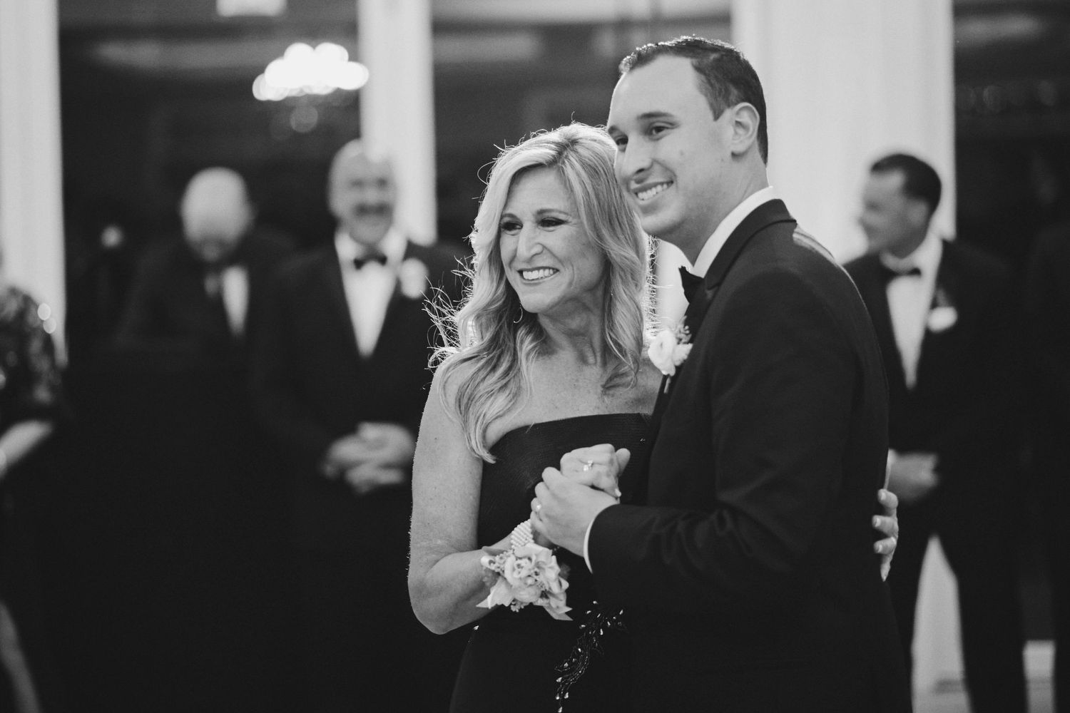 A joyful couple smiles and laughs together during a formal black-tie event in black and white photography.