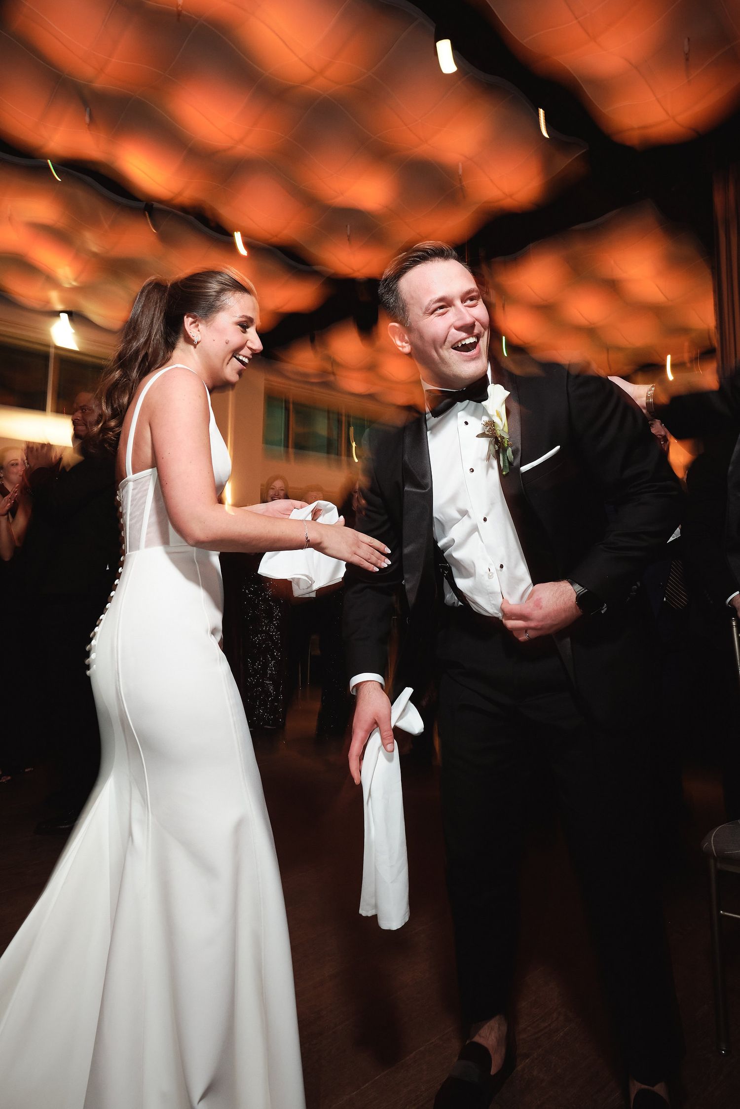 A bride and groom share a joyful moment on the dance floor under warm amber lighting at their wedding reception.
