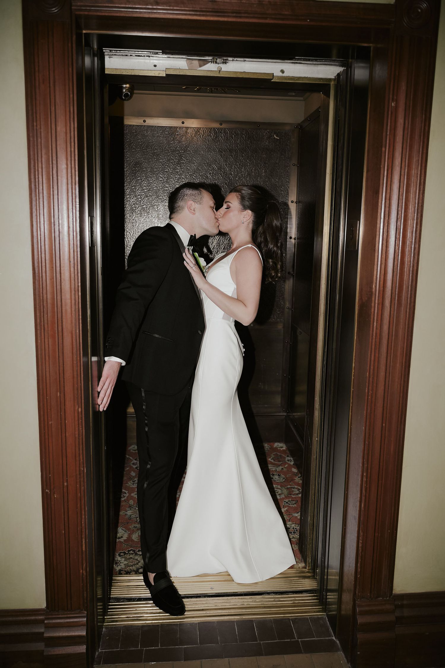 A couple in wedding attire share a romantic moment while standing in an elegantly framed doorway.