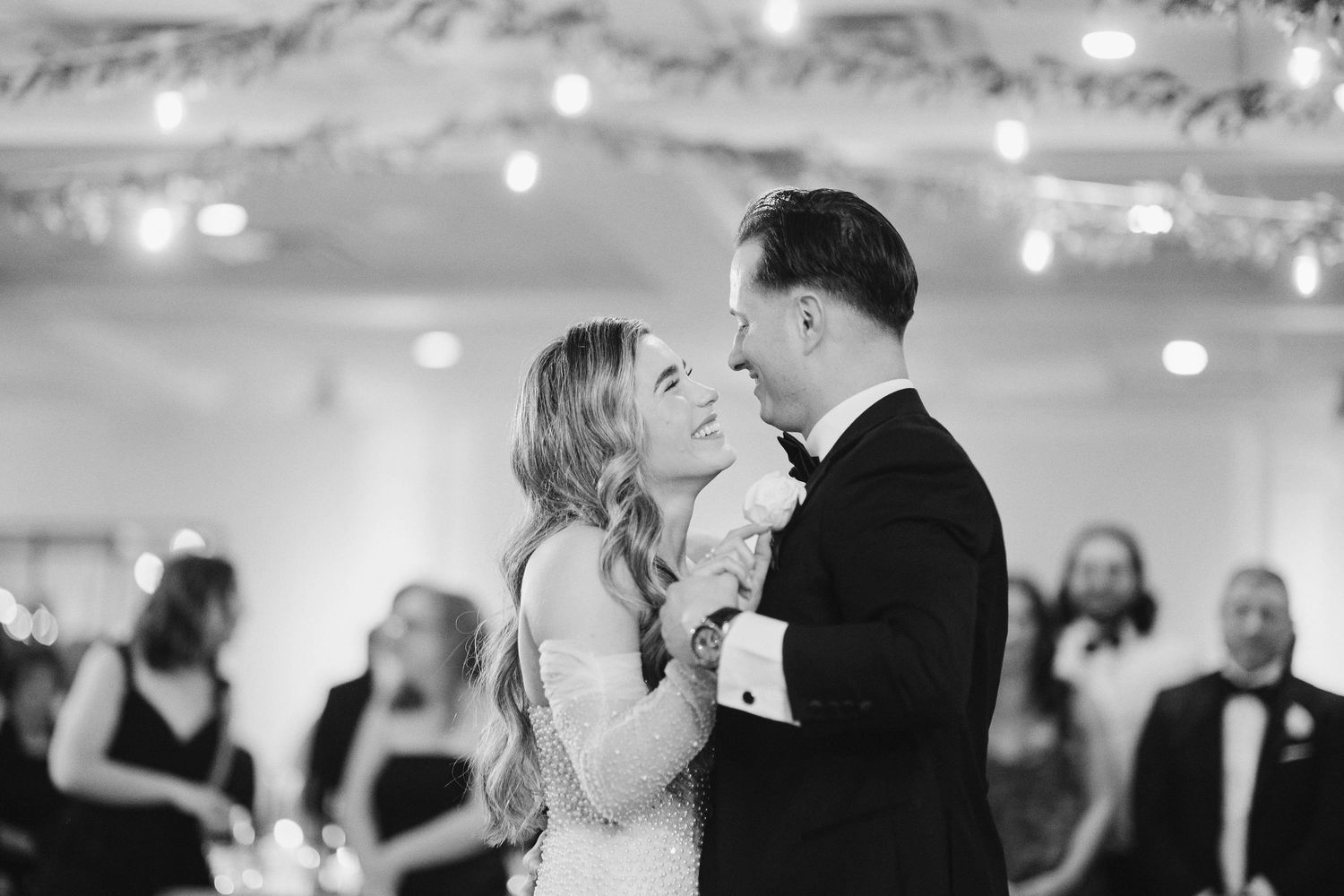 A couple shares their first dance together at an elegant indoor wedding reception with glowing lights in the background.