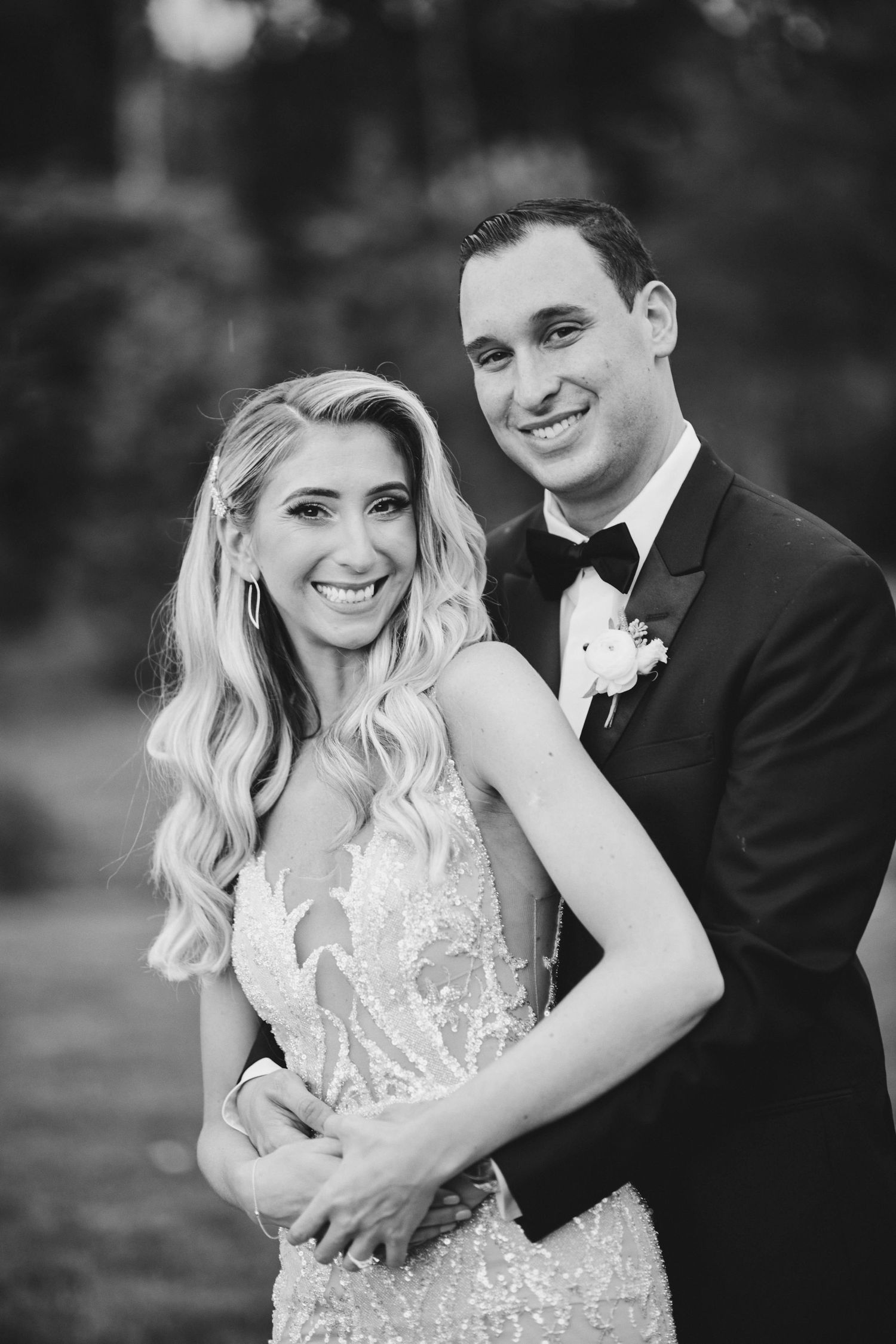 Black and white portrait of a newlywed couple in formal attire, with the bride wearing a lace dress and groom in tuxedo.