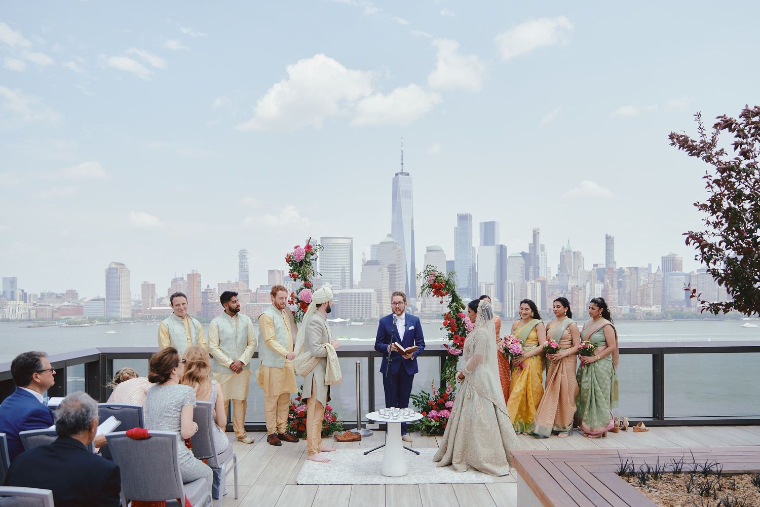 Wedding ceremony taking place on rooftop terrace with New York City skyline and Freedom Tower in background.