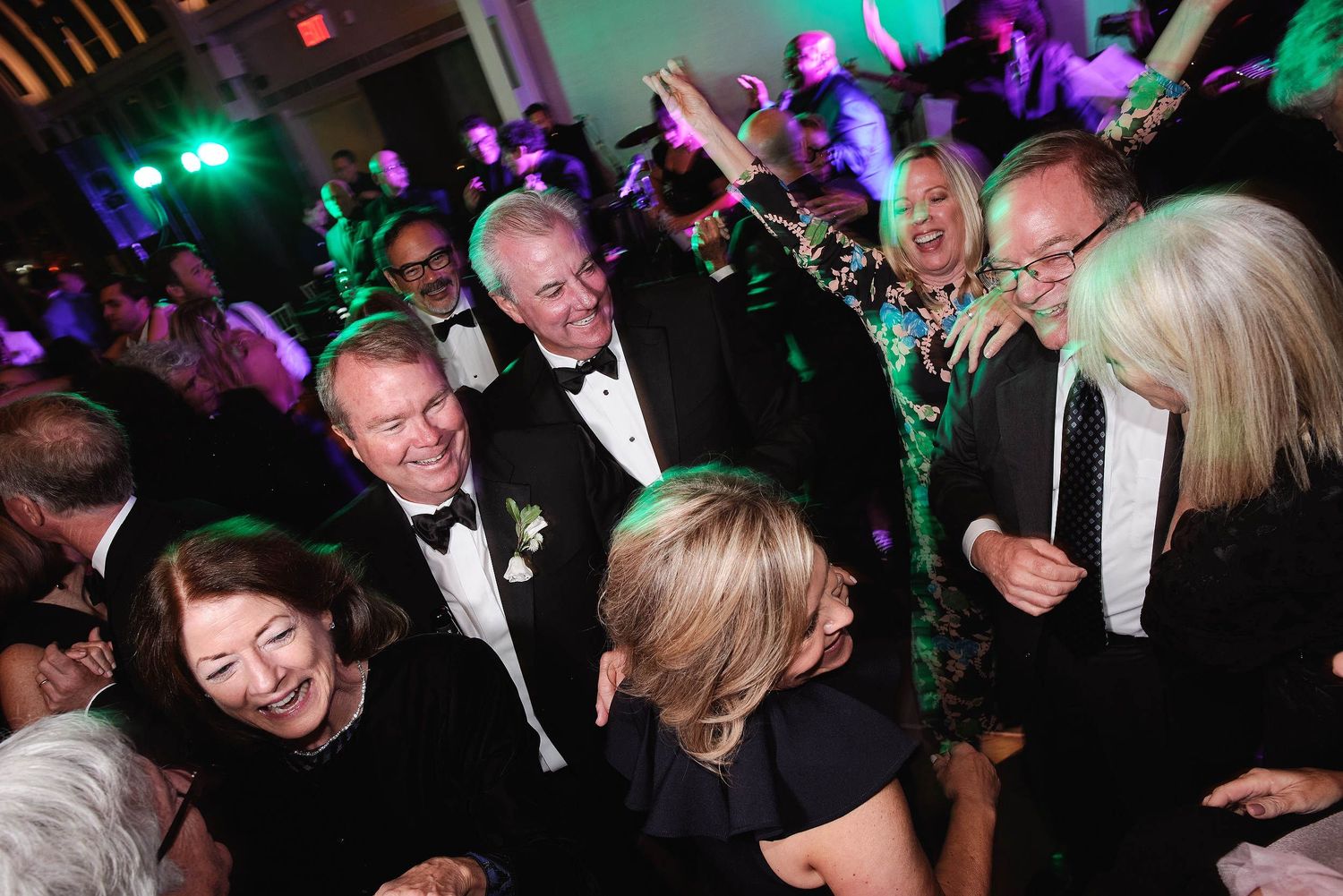 People enjoying a lively party scene with colorful lights and formal attire on a dance floor.