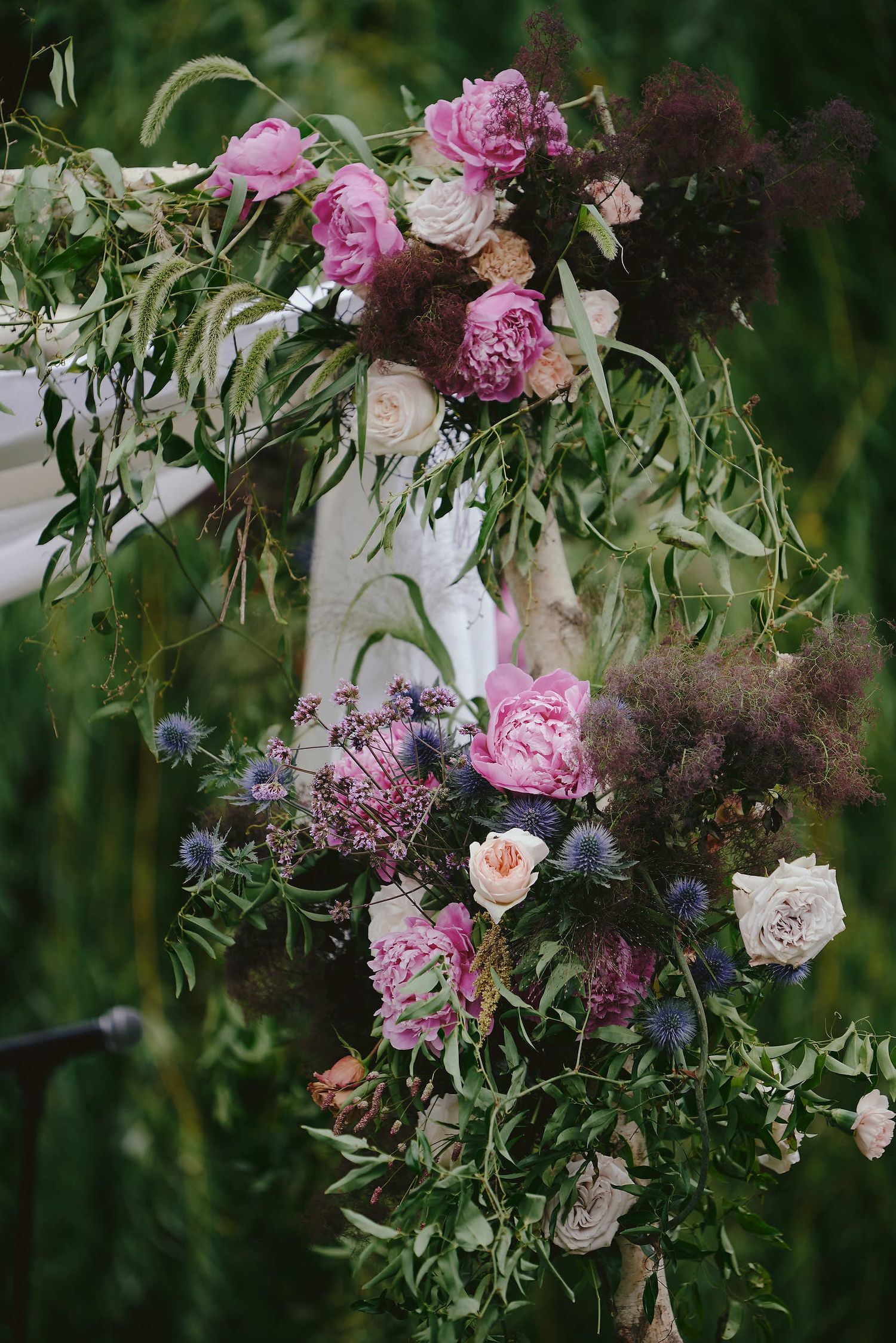Romantic floral arrangement featuring pink peonies, white roses, and wispy greenery cascading down in a natural garden setting.