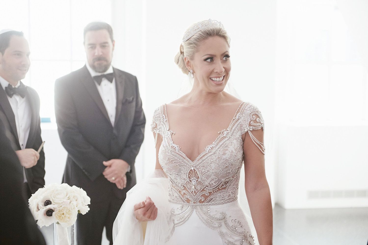 A wedding party scene during a joyful moment, with the bride wearing an elegant lace V-neck gown.