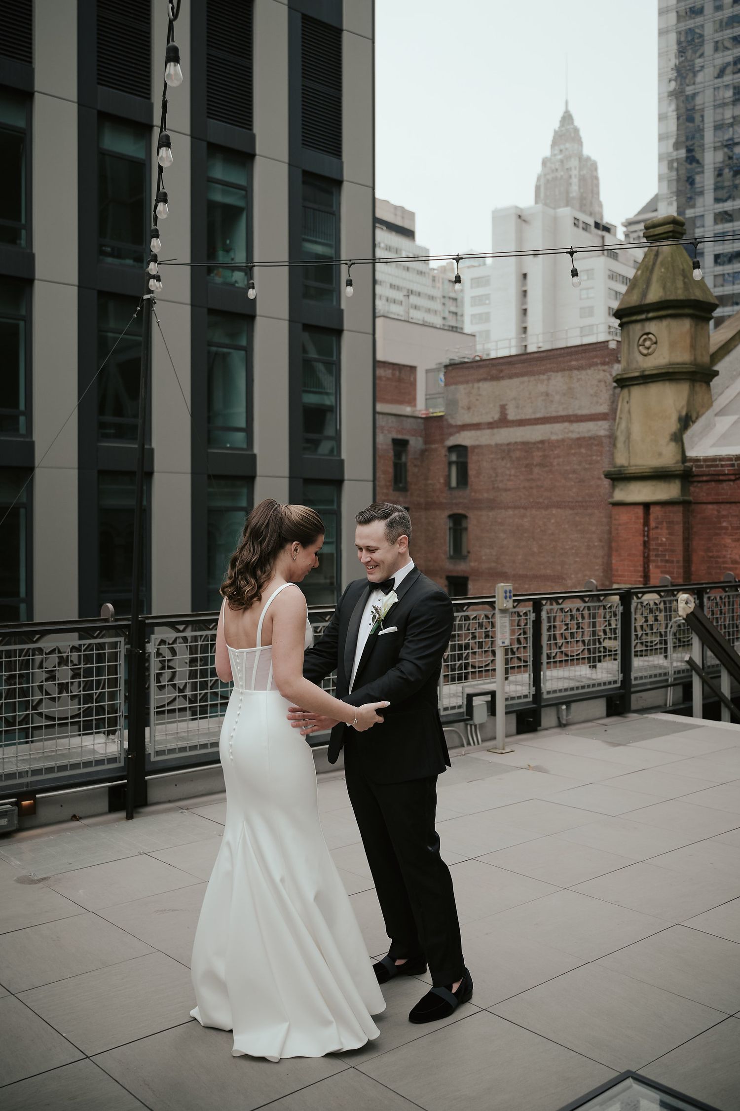 A bride and groom share a private moment on an urban rooftop with city architecture in background.