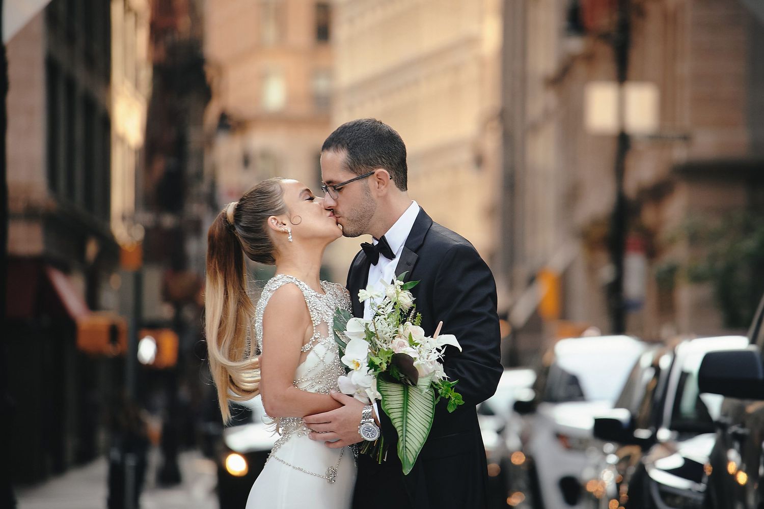 A romantic wedding moment on a city street with a white bridal bouquet featuring lilies and greenery.
