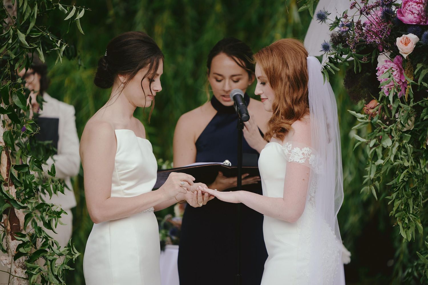 Wedding ceremony under a floral arch with delicate pink roses and greenery.