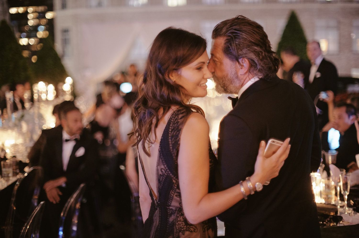 A couple shares a romantic dance at an elegant evening reception with candlelit tables and formal decor.