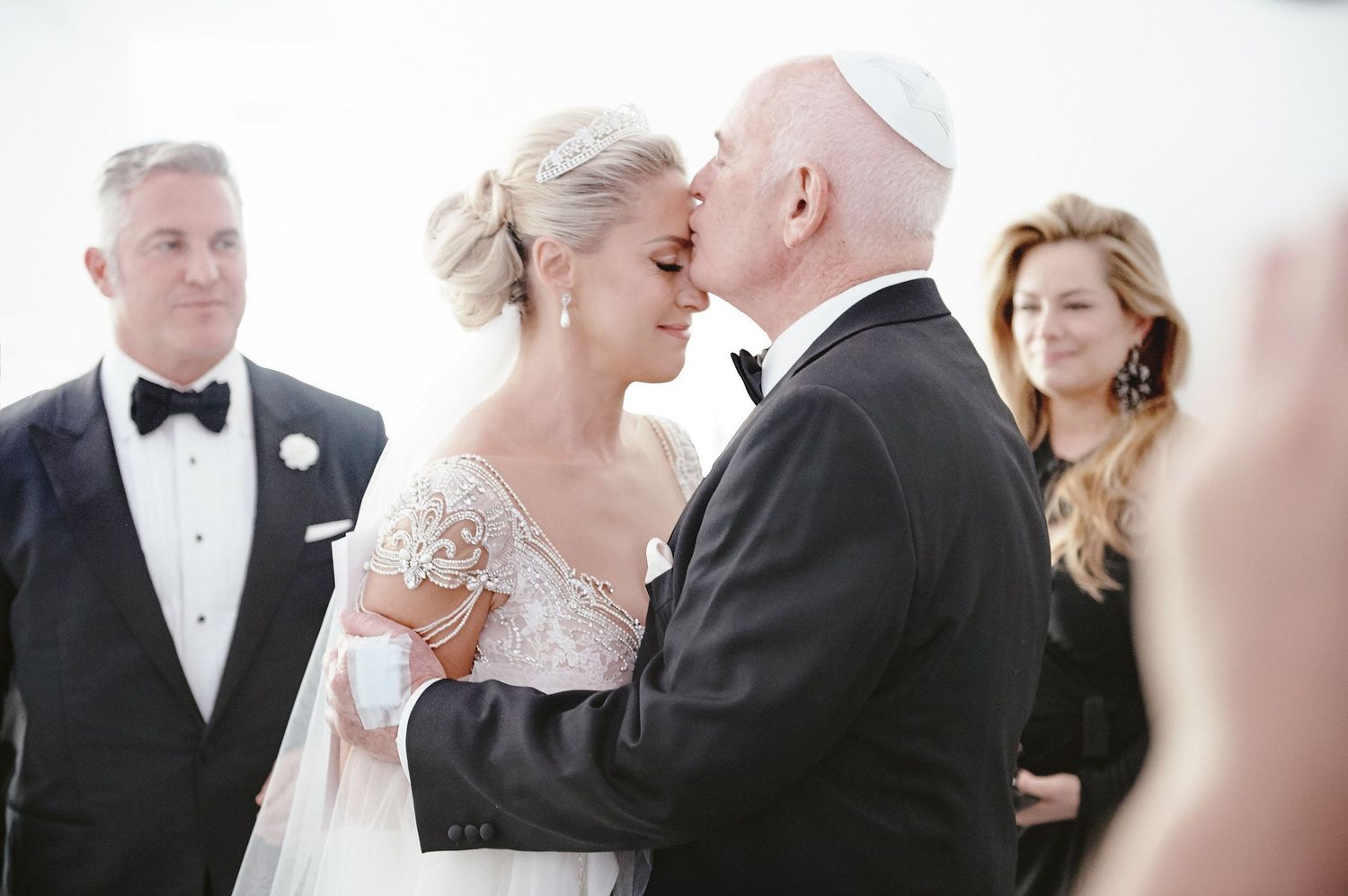 A tender moment between two people during a formal wedding ceremony with black tie attire and elegant decor.