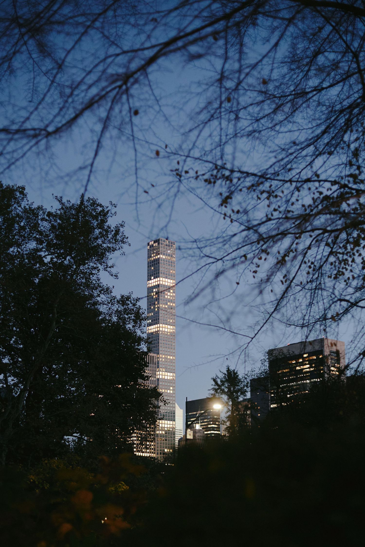 View of 432 Park Avenue luxury skyscraper at dusk through tree branches in New York City.