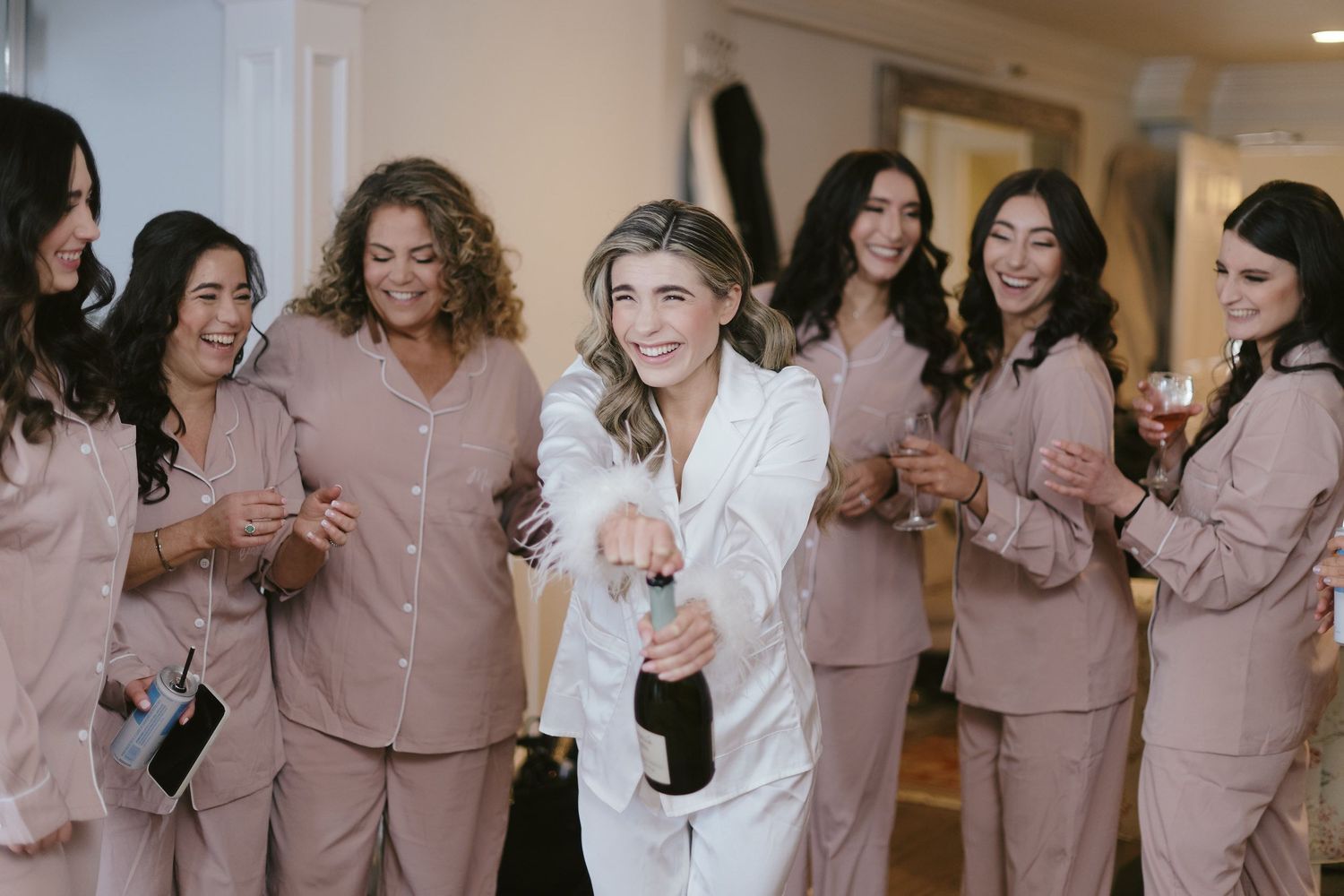 Wedding party getting ready in matching satin pajama sets with champagne celebration in hallway.
