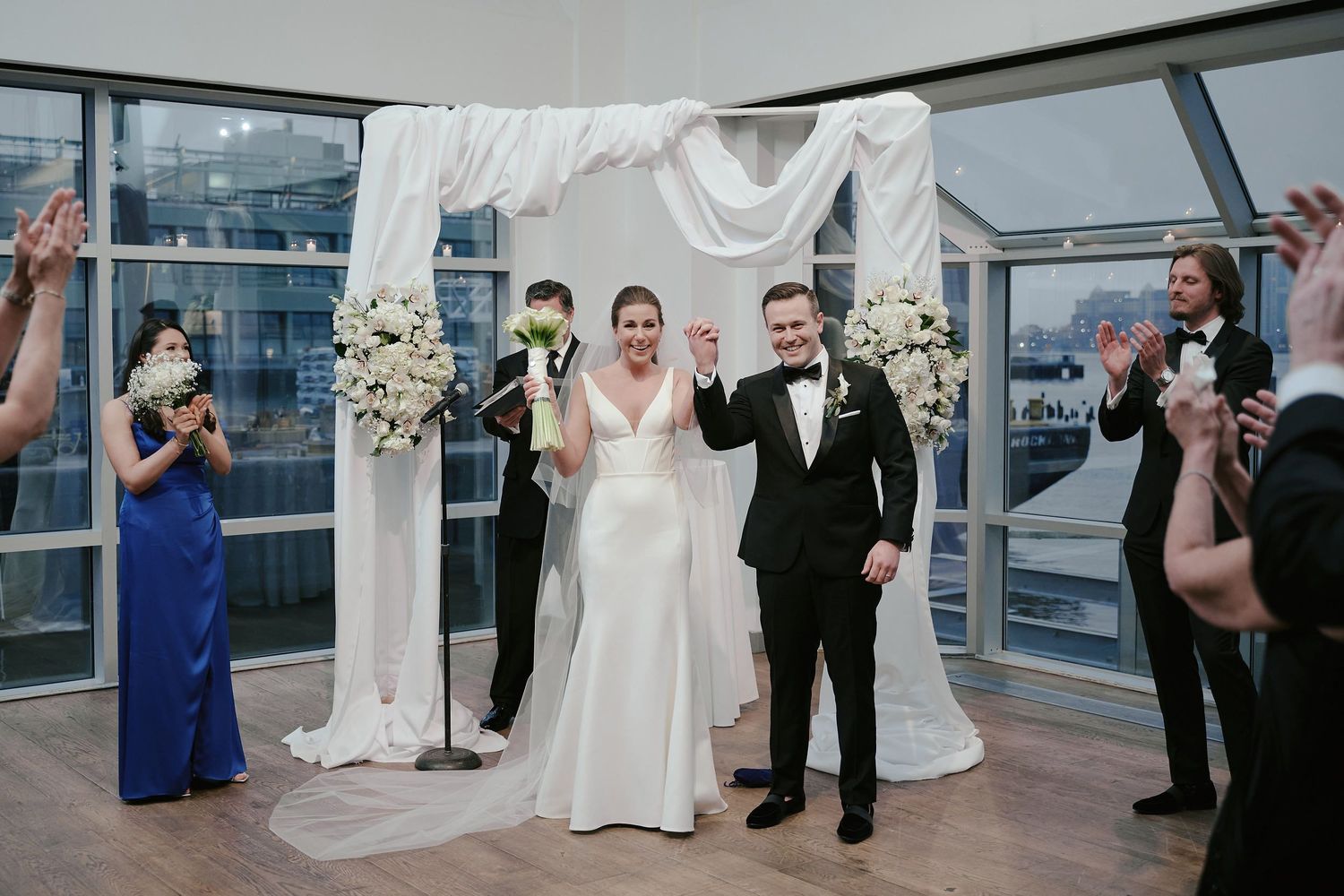 Wedding ceremony on a rooftop venue with white floral arch and guests in formal attire celebrating the occasion.