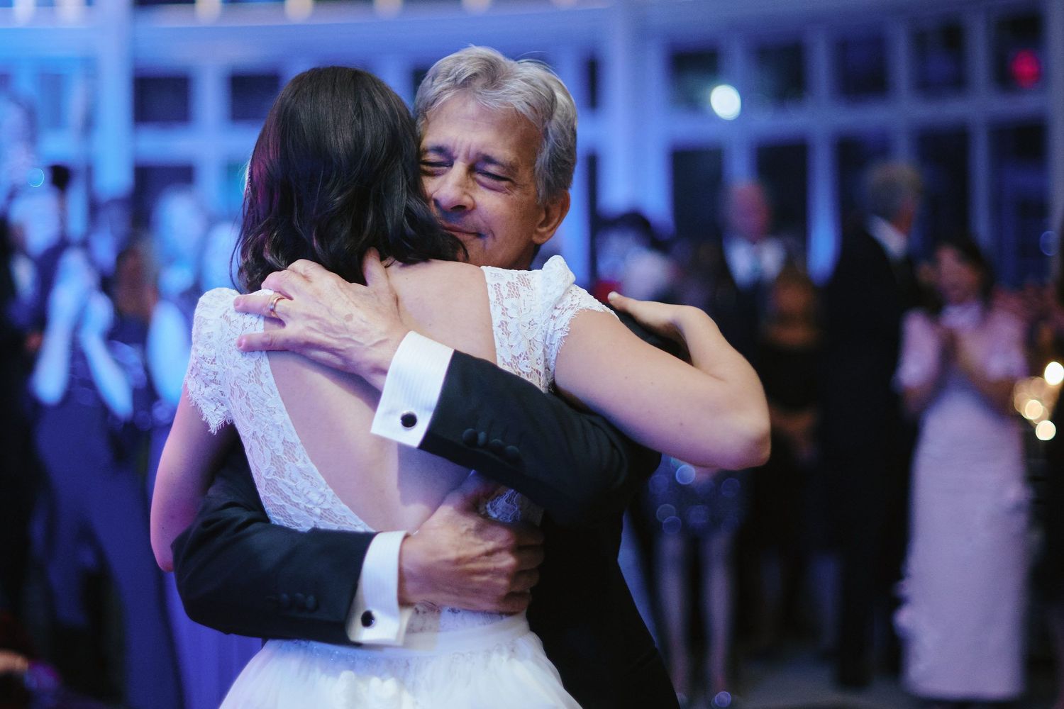 A bride and groom share an intimate embrace during their first dance at a wedding reception with blue lighting.